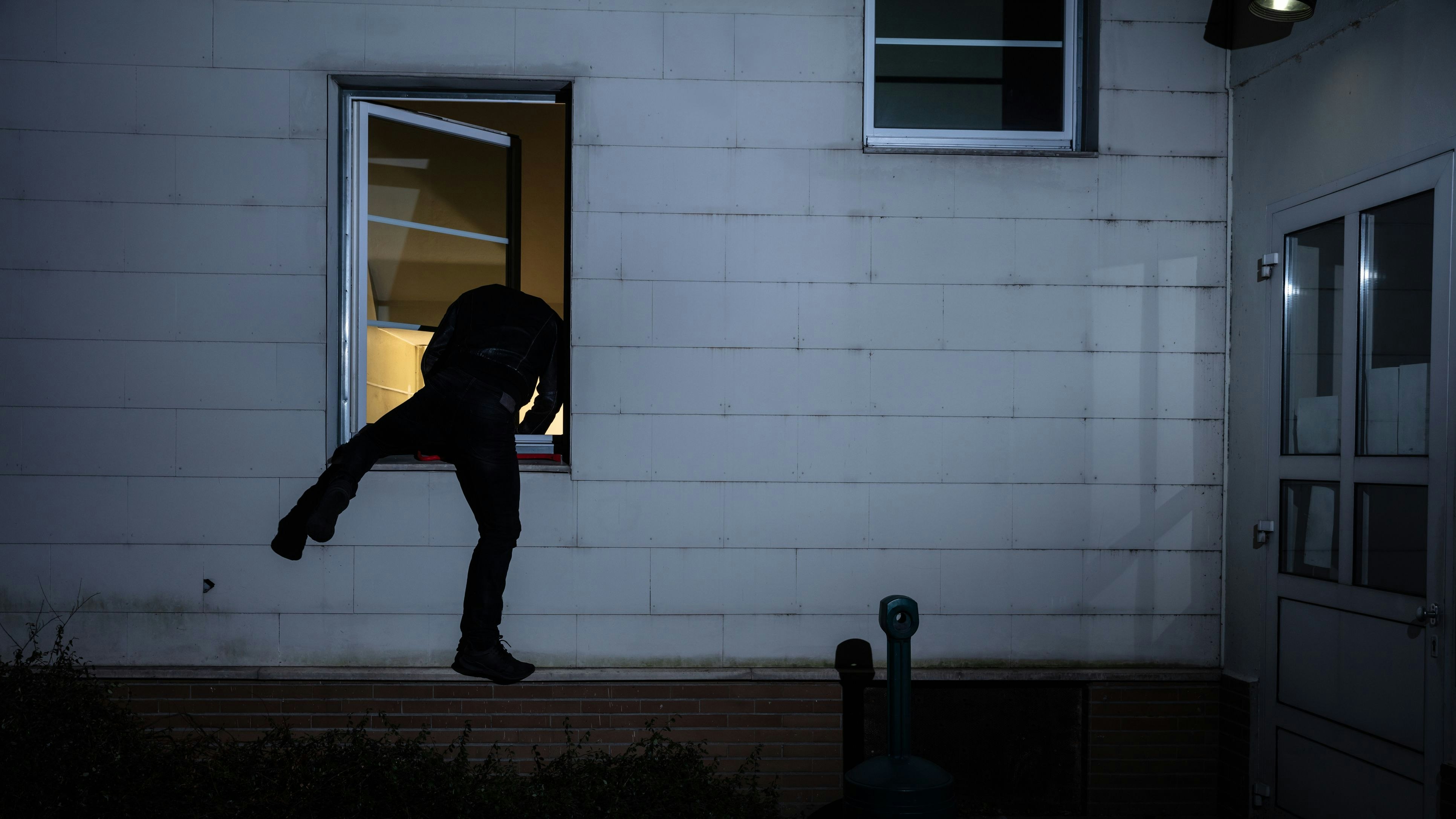 Rear View Of A Burglar Entering In A House Through A Window