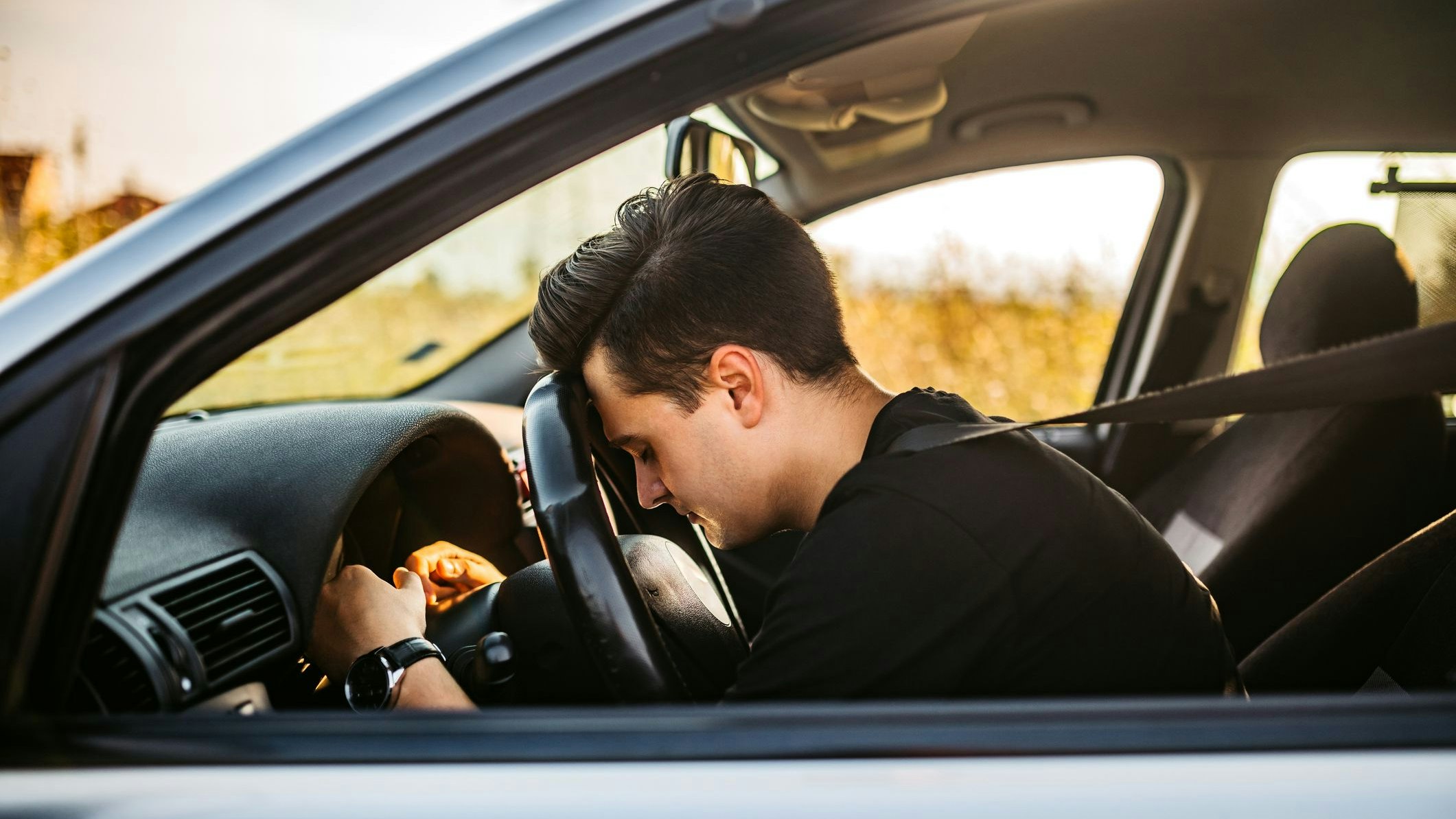 Young, handsome tired man sleeping on steering wheel in car.