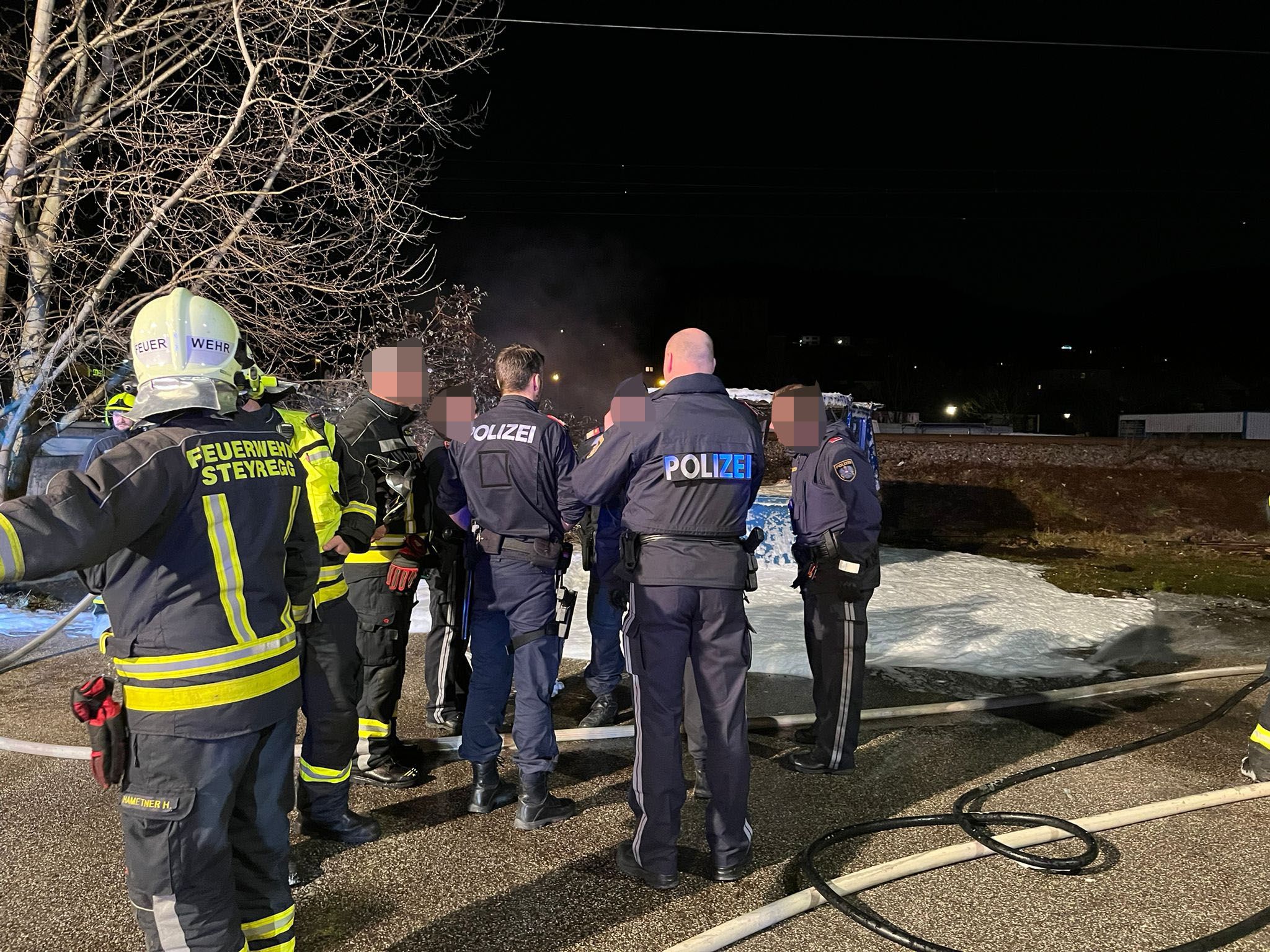 Einsatzkräfte von Feuerwehr und Polizei nach dem Brand vor der Asylunterkunft in Steyregg (Bez. Urfahr-Umgebung).