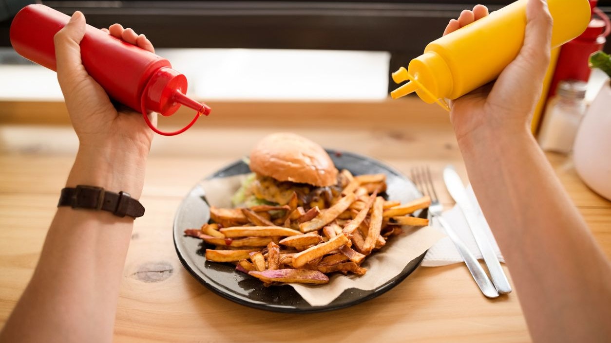 Point of view shot of a woman adding mustard and ketchup to french fries at a restaurant