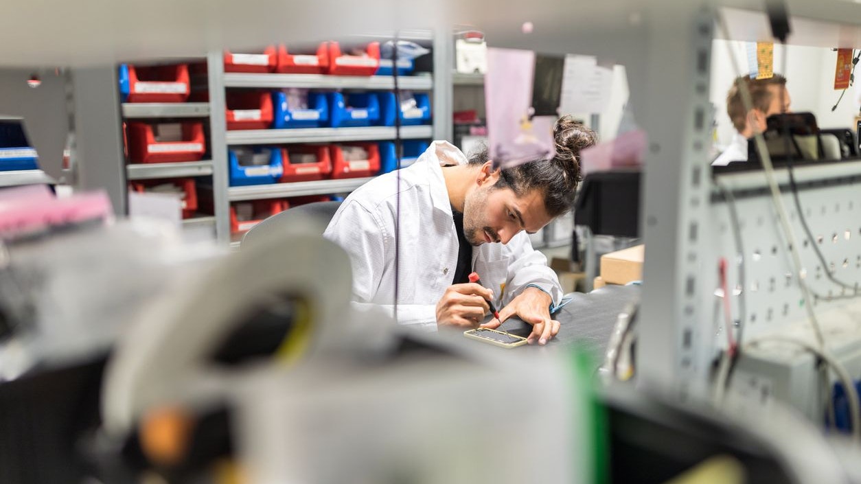 Male technician fixing a mobile device in a repair workshop. Technician repairing a mobile phone in service center.