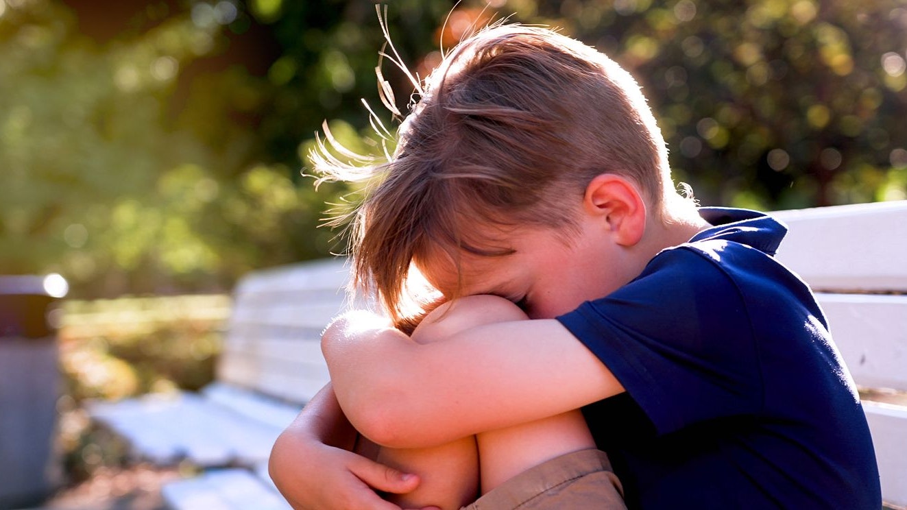 Crestfallen Crying child boy sitting on a bench covering his face