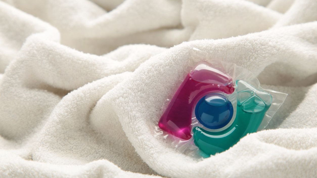 Washing gel capsule pods with laundry detergent on a pile of white cloth background.