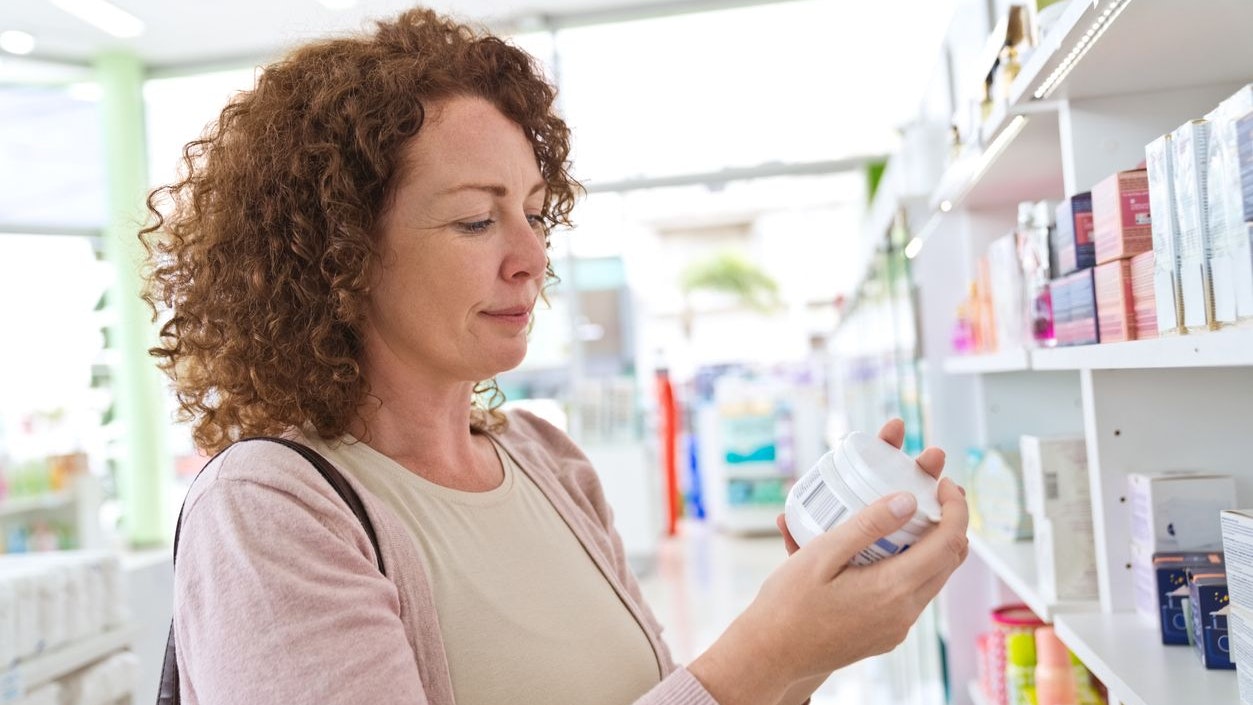 Female customer wearing light pink blouse choosing cosmetics in pharmacy.