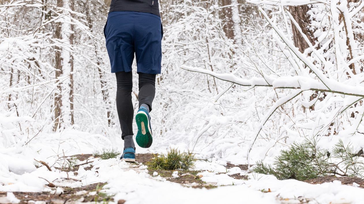 The young man is running on a forest road during winter. The man trains outdoors far from the city. The forest is covered in snow after a snowfall.