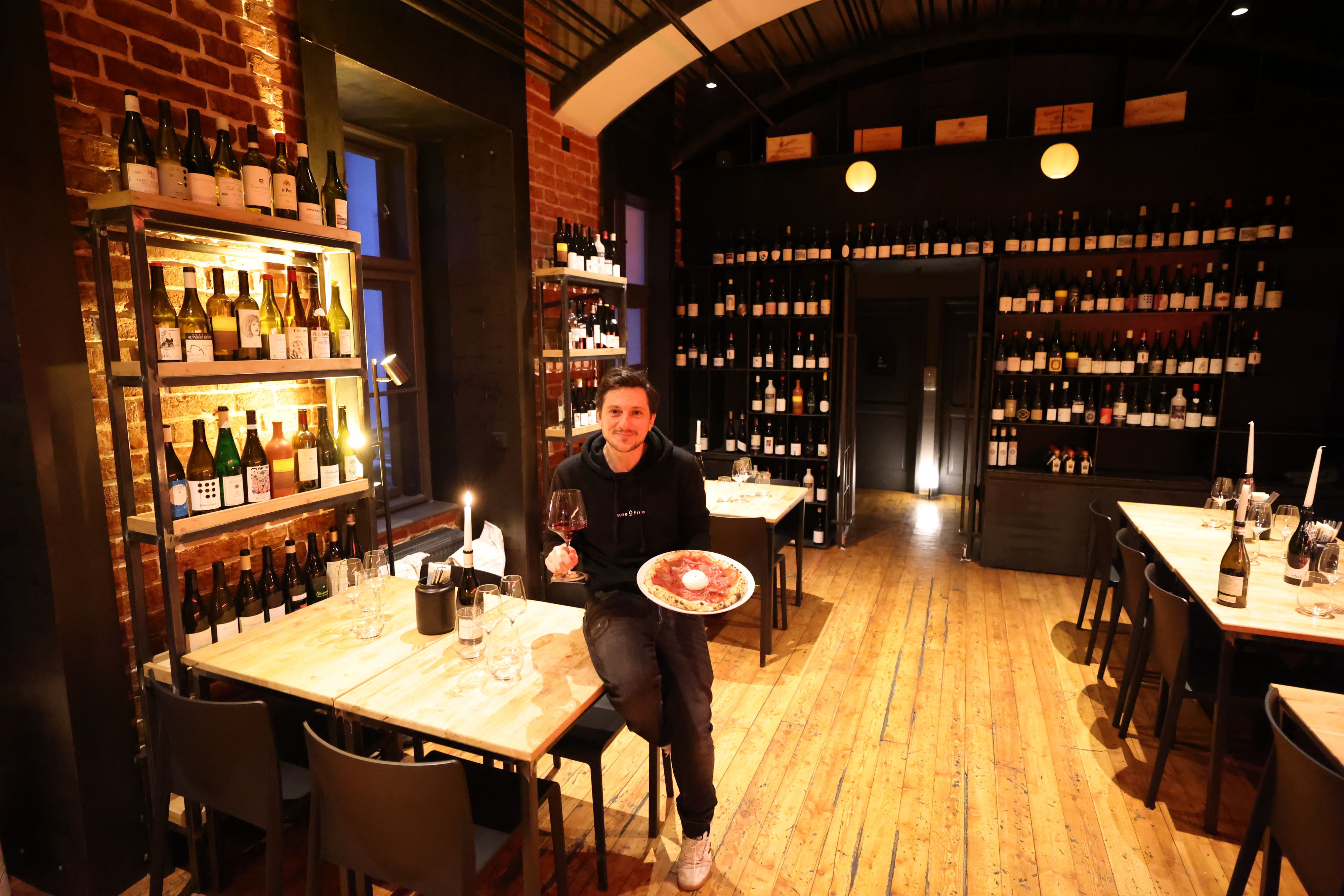 Rainer Ziegler mit Rinderschinken-Pizza an Büffelmozarella. Im Hintergrund ein Ausschnitt aus seiner umfangreichen Weinauswahl