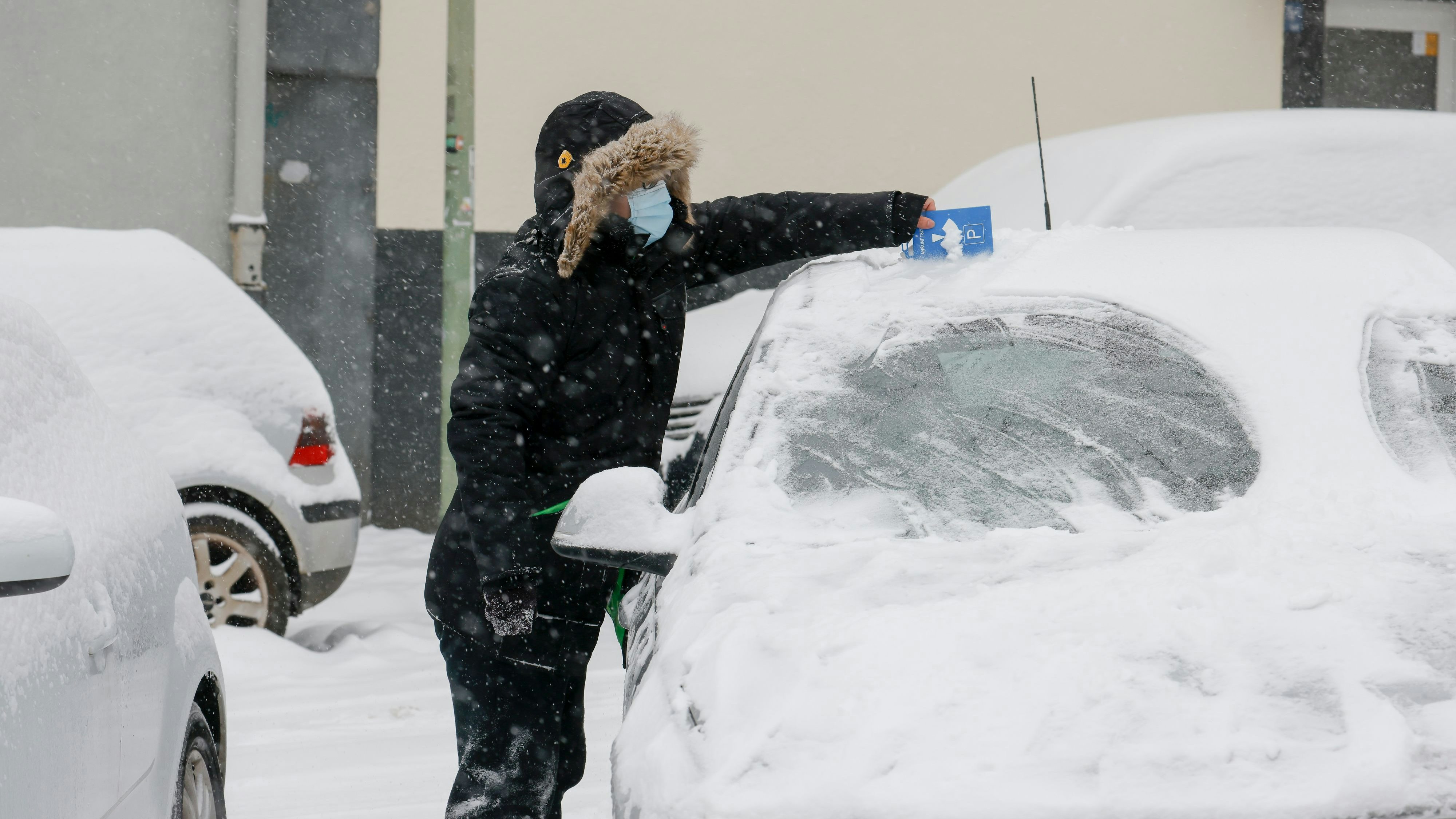 Pkw-Besitzer kratzen das Eis von ihren Fahrzeugen.