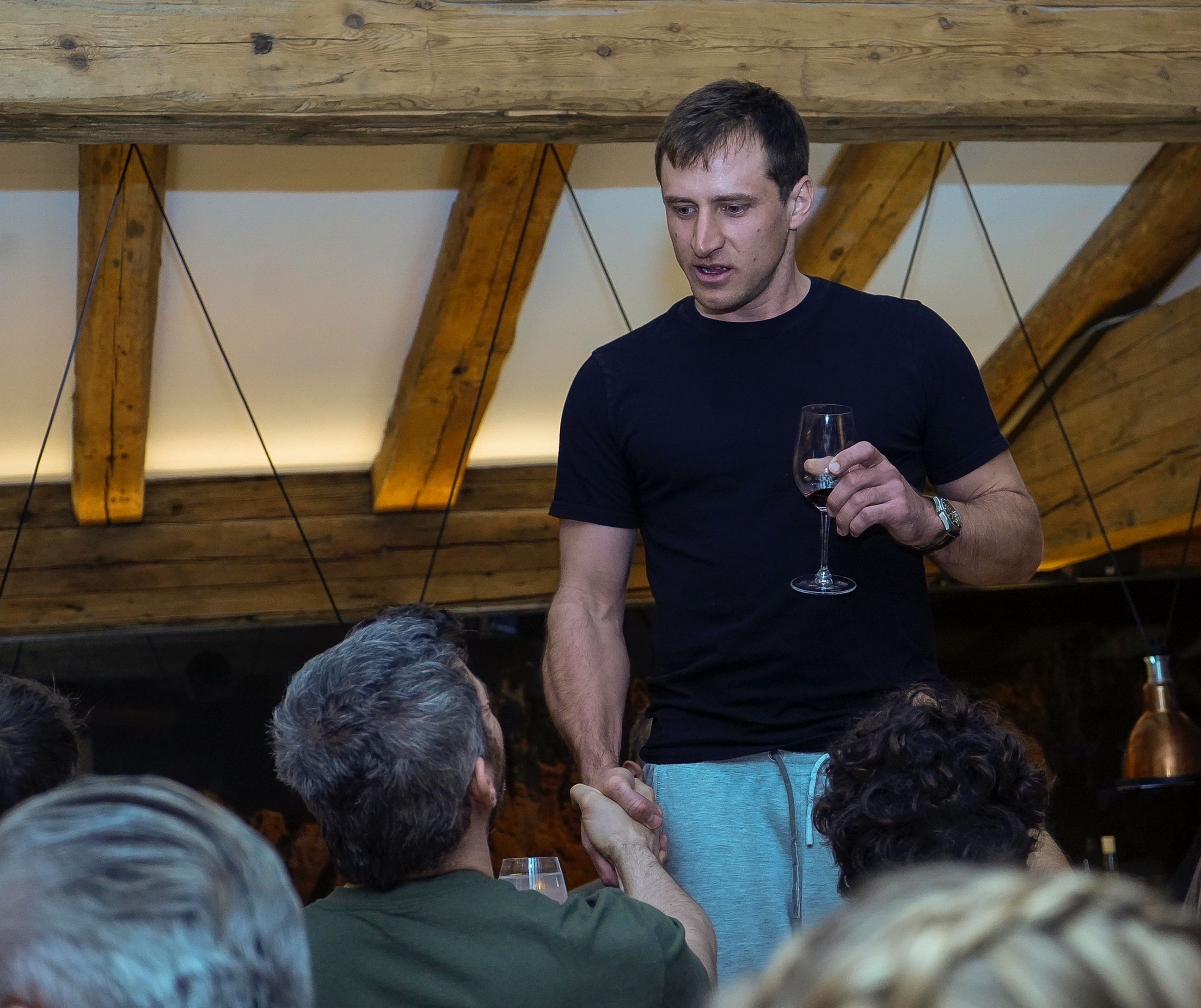 ÖSV-Legende Mayer grüßt am Tisch stehend mit einem Rotweinglas in der Hand einen Gast.&nbsp; &nbsp;