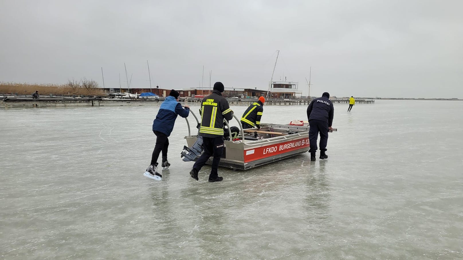 Eisläufer schieben die Boote über die Eisfläche am Neusiedler See.