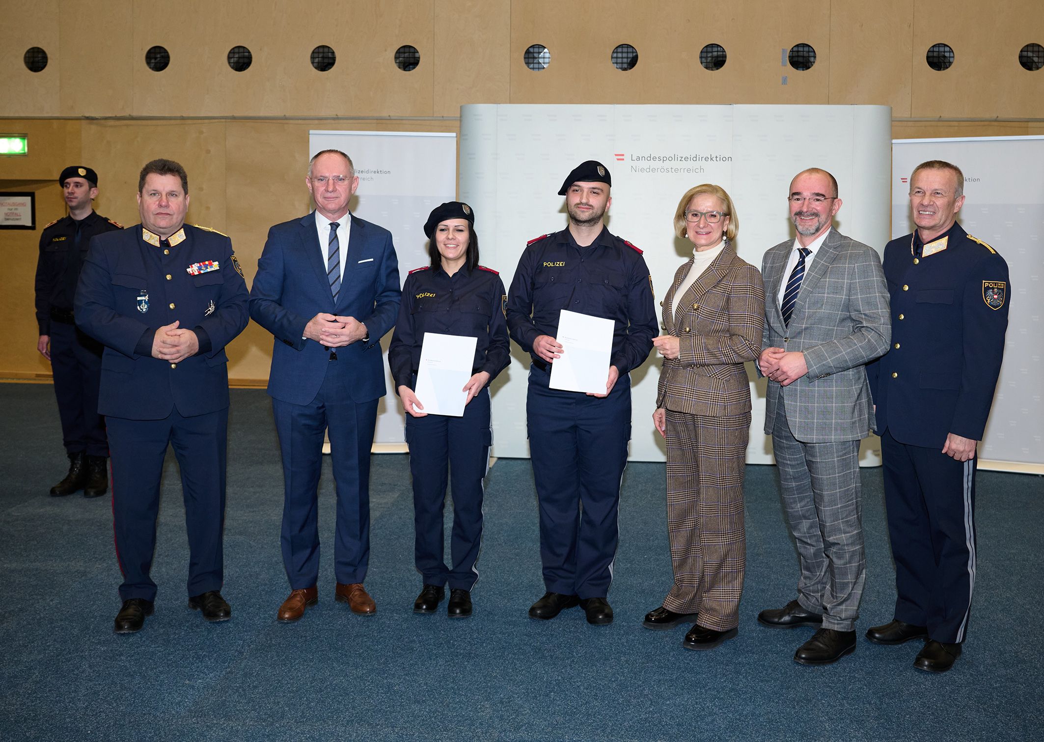 Bundespolizeidirektor Michael Takacs, Innenminister Gerhard Karner, Kerstin Karner, Emre Cakir, Landeshauptfrau Johanna Mikl-Leitner, Sektionschef Karl Hutter und Landespolizeidirektor Franz Popp bei der Übergabe der Dienstprüfungszeugnisse.