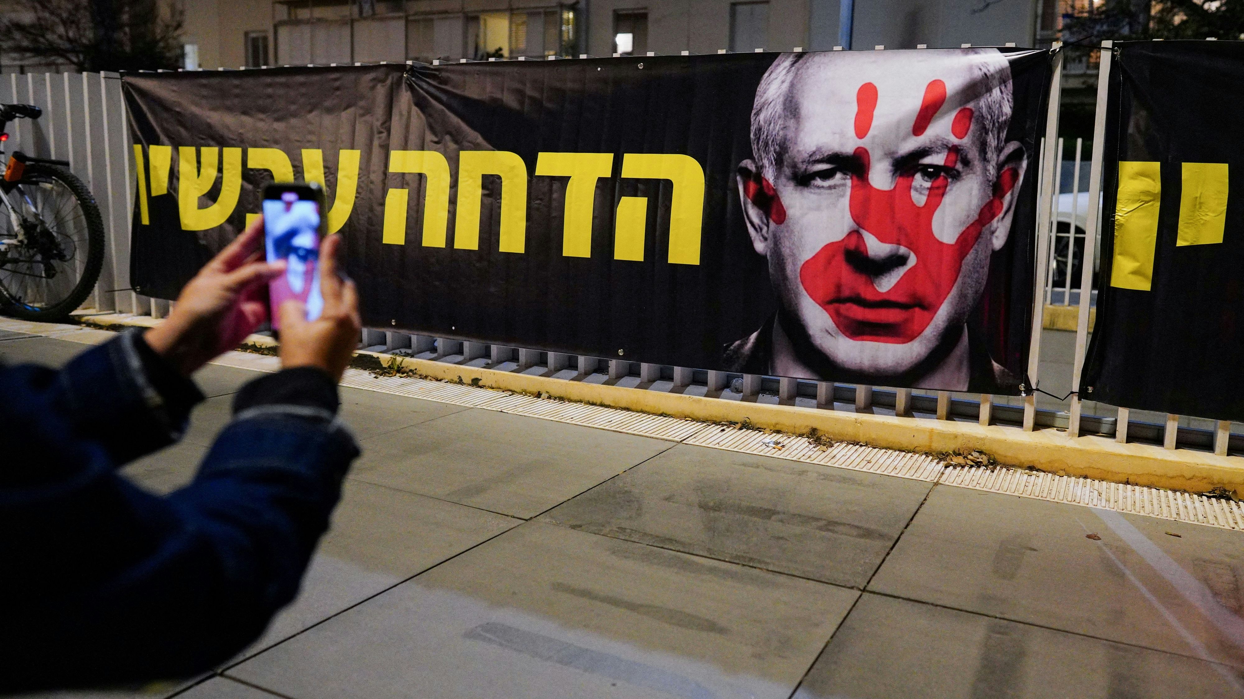 A person takes a picture of a banner, during a protest against Israeli Prime Minister Benjamin Netanyahu's government in Tel Aviv, Israel, January 20, 2024. REUTERS/Alexandre Meneghini 