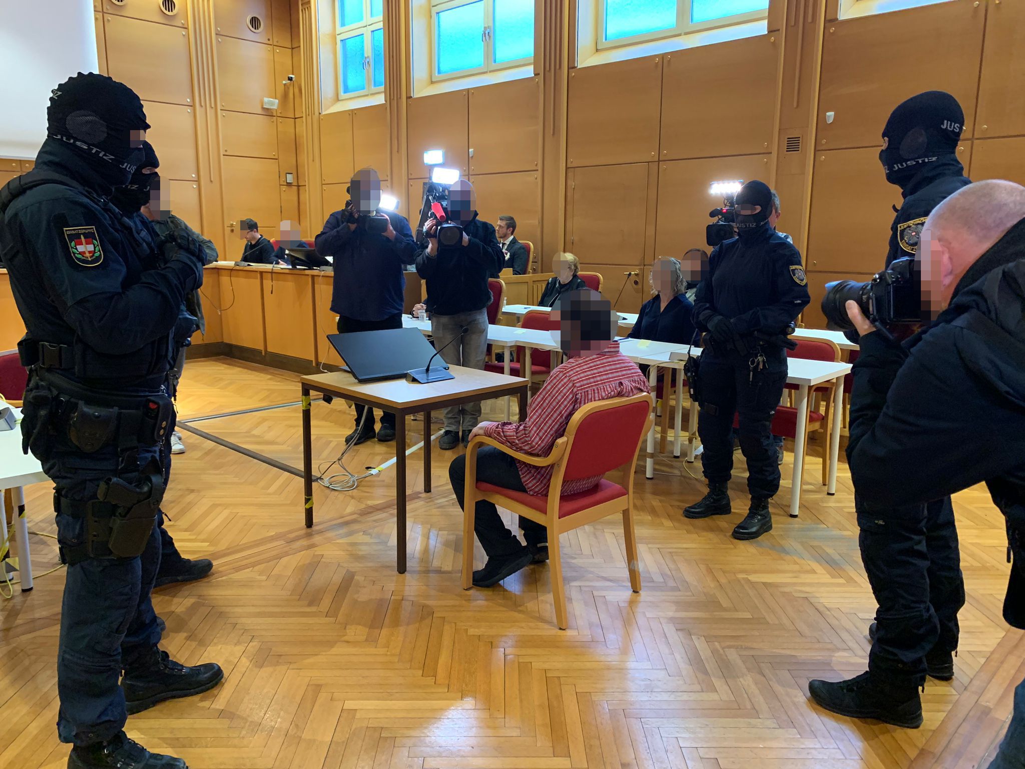 Der Verdächtige erschien in einem rotkarierten Hemd. Er wird schwer bewacht von mehreren Beamten.