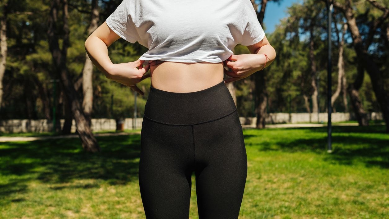 Young sportive woman wearing black yoga pant and white tees standing on a park bench.