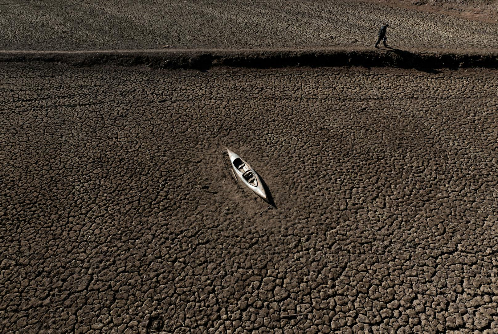 Wassernotstand: Den Großraum Barcelona plagt eine historische Dürre. Ein Mann geht an einem verlassenen Kanu am Sau-Stausee vorbei. Hier war mal Wasser.