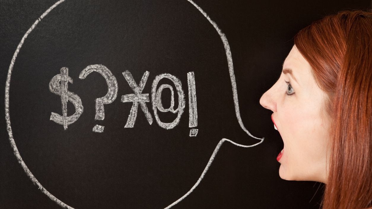 A woman stands by a chalk drawn talk bubble with swear symbols in it.
