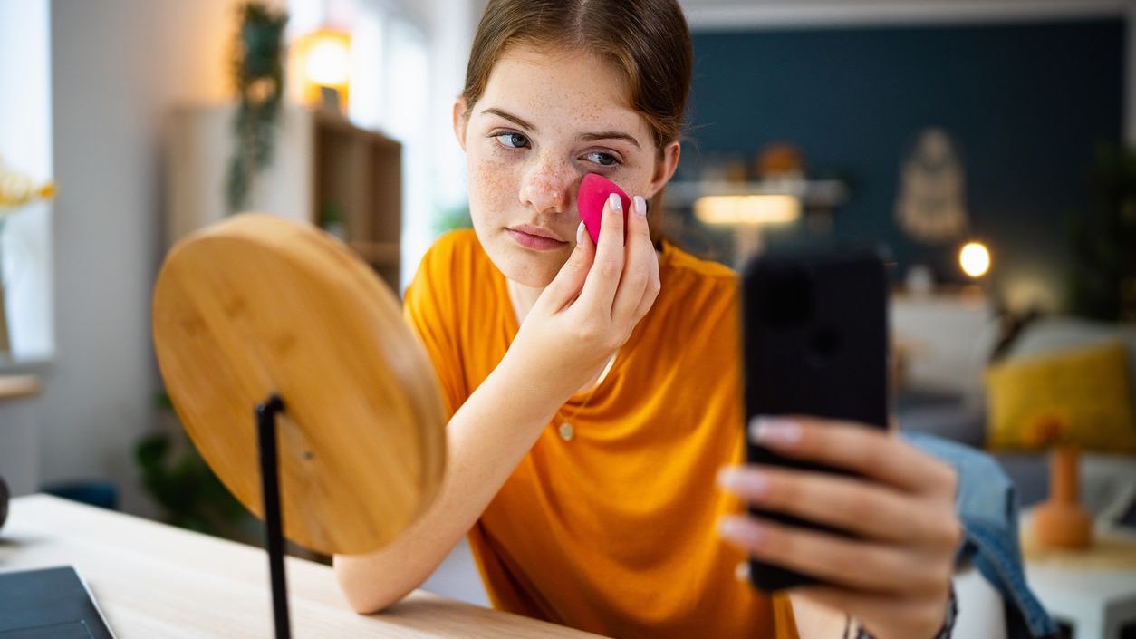 Teenage girl texting messages on her phone while doing make-up.