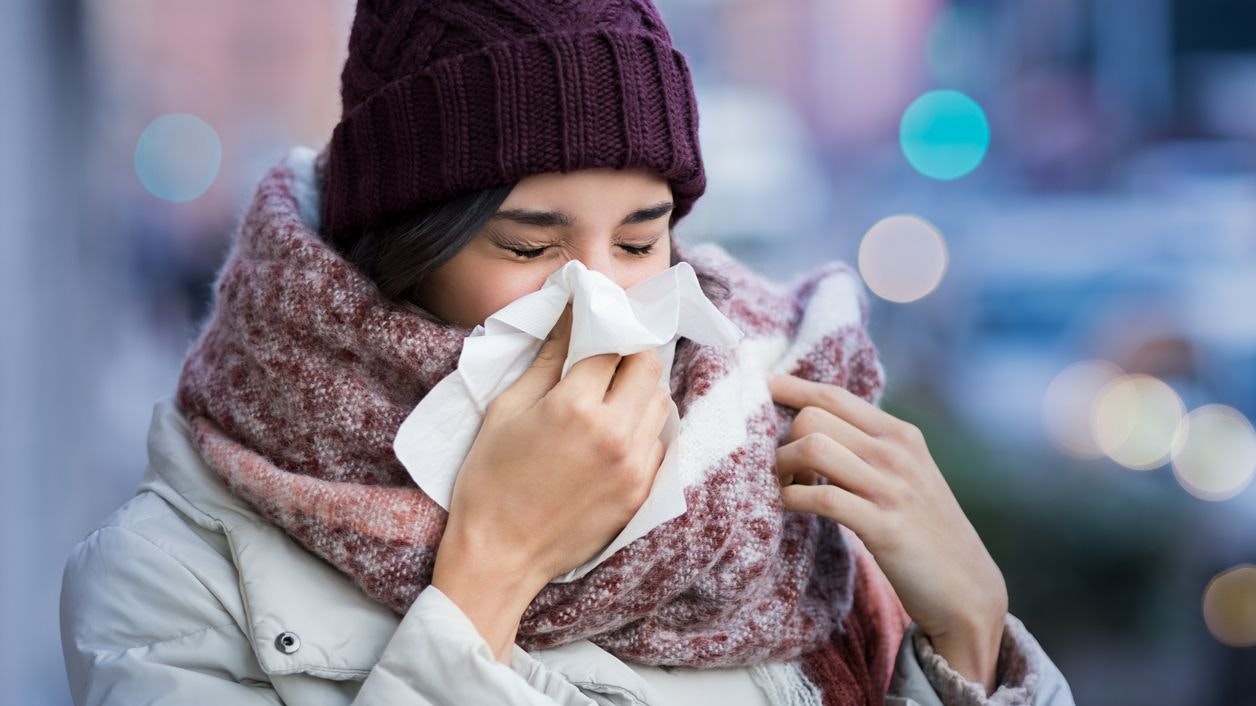 Pretty young woman blowing her nose with a tissue outdoor in winter. Young woman getting sick with flu in a winter day. Woman with a cold.
