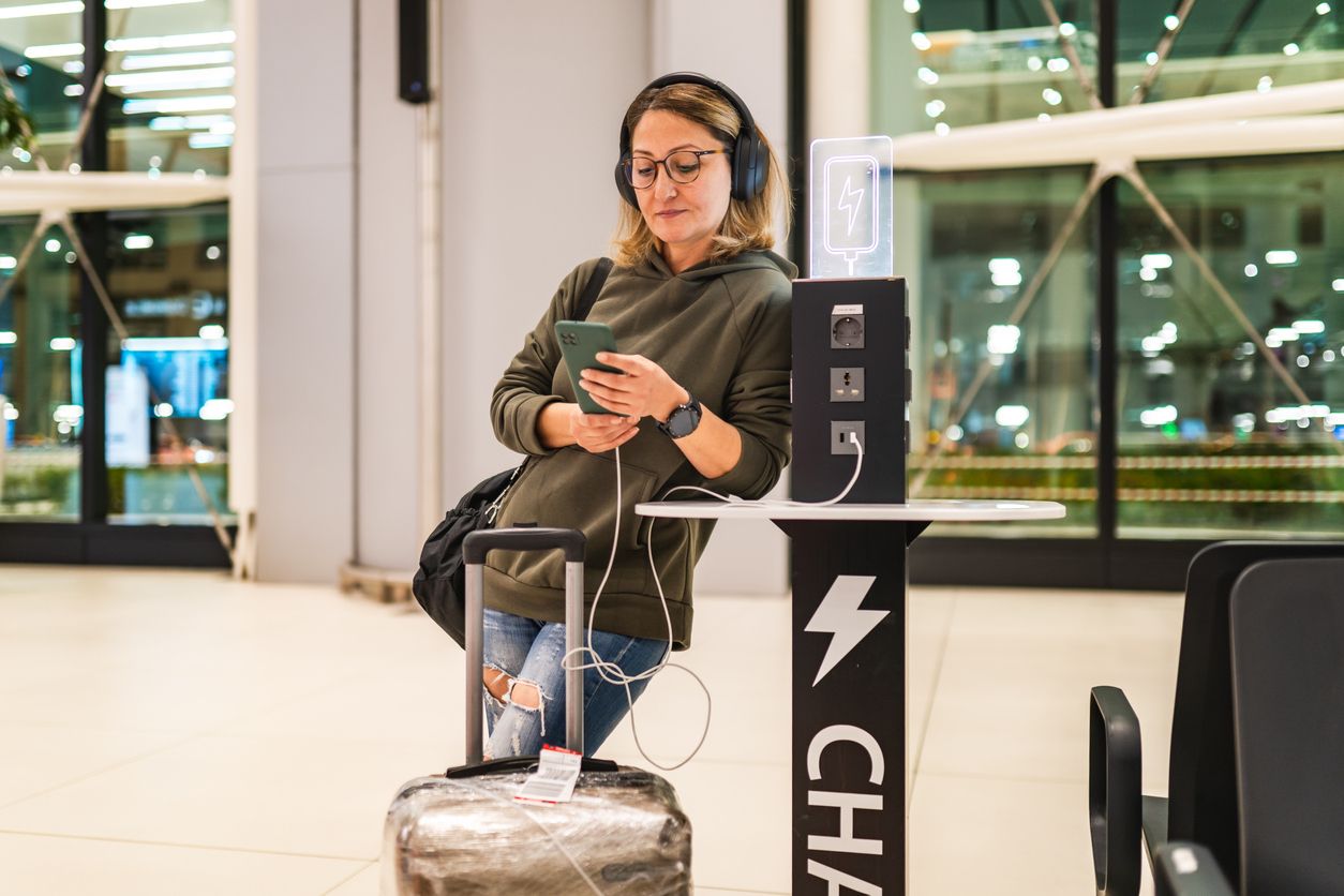 Woman waiting for her flight at the airport while charging her phone at charging station