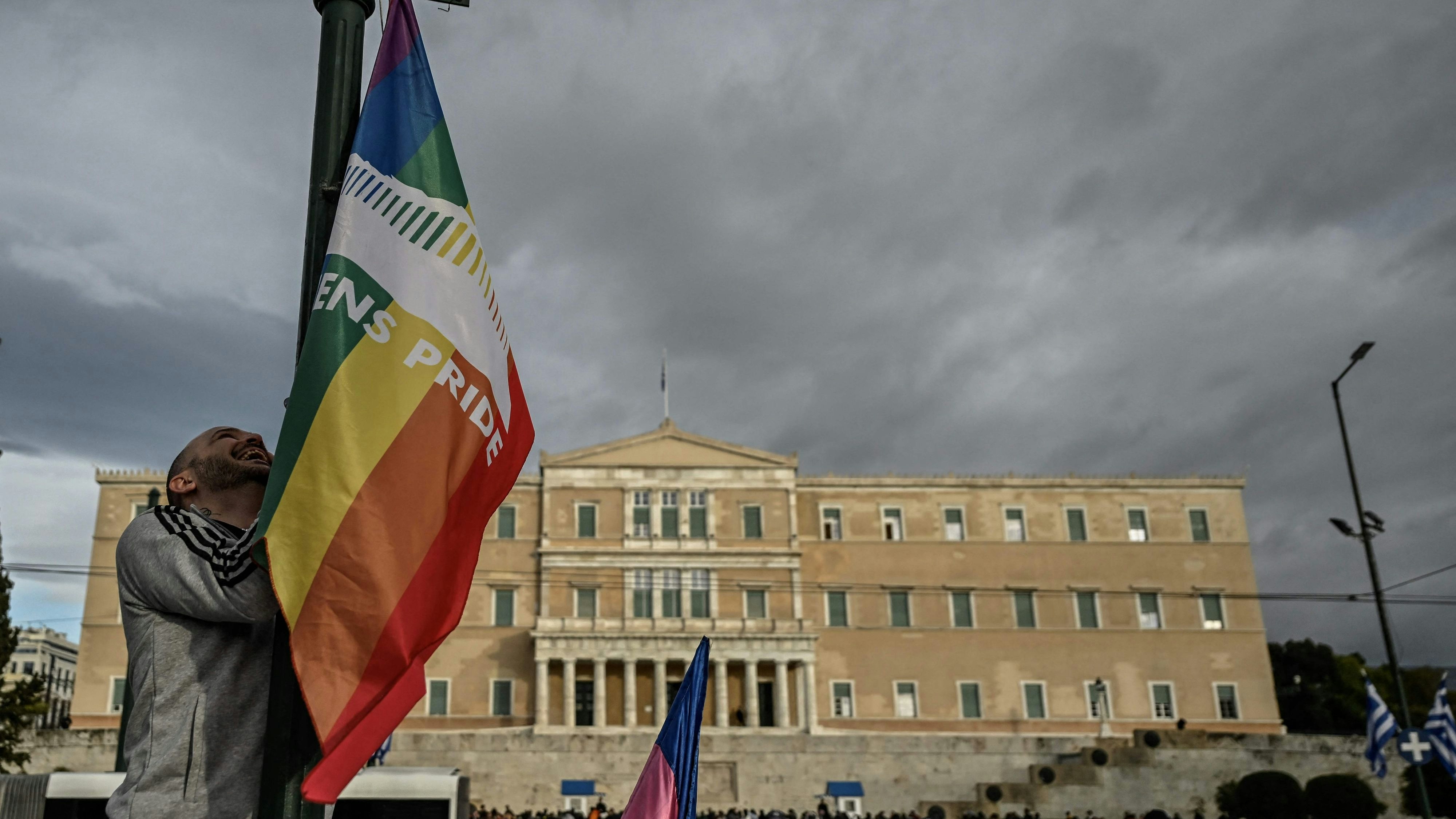 Download von www.picturedesk.com am 16.02.2024 (09:32).  A person hangs a LGBTQ pride flag on a light pole outside the Greek Parliament during a gathering with fellow supporters of the LGBTQ community as lawmakers vote on a same-sex marriage and adoption for same-sex couples bill on February 15, 2024 in Athens. Greece's Parliament was set to legalise same-sex marriage and adoption today, a landmark reform promoted by the conservative government over the opposition of the country's powerful Orthodox Church. (Photo by Aris MESSINIS / AFP) - 20240215_PD9202 - Rechteinfo: Rights Managed (RM) Nur für redaktionelle Nutzung! Werbliche Nutzung erfordert Freigabe: bitte schicken Sie uns eine Anfrage.