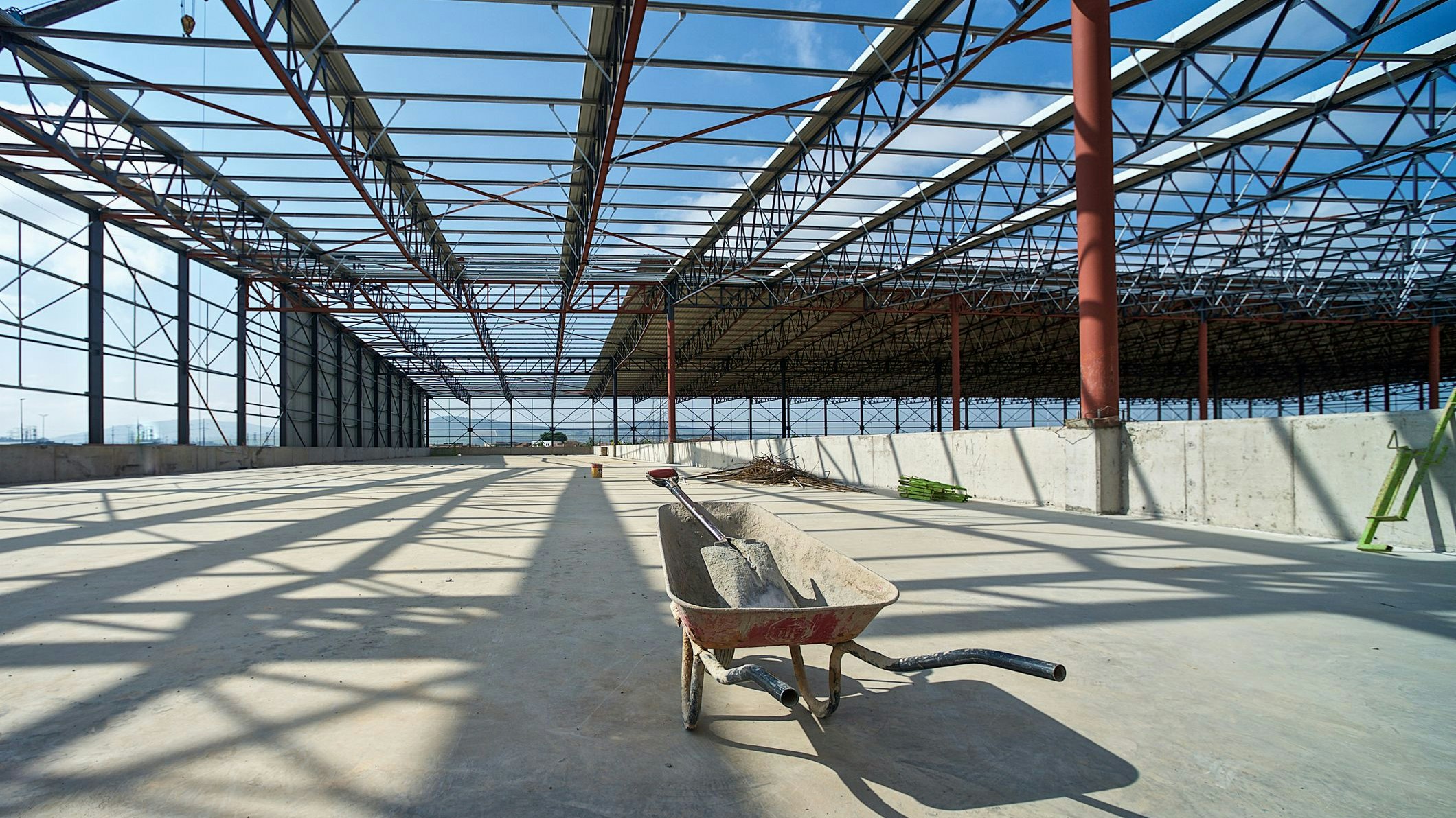 A wheelbarrow with a shovel in on the concrete deck of a an empty construction warehouse site with structural beams prior to decking in Cape Town South Africa