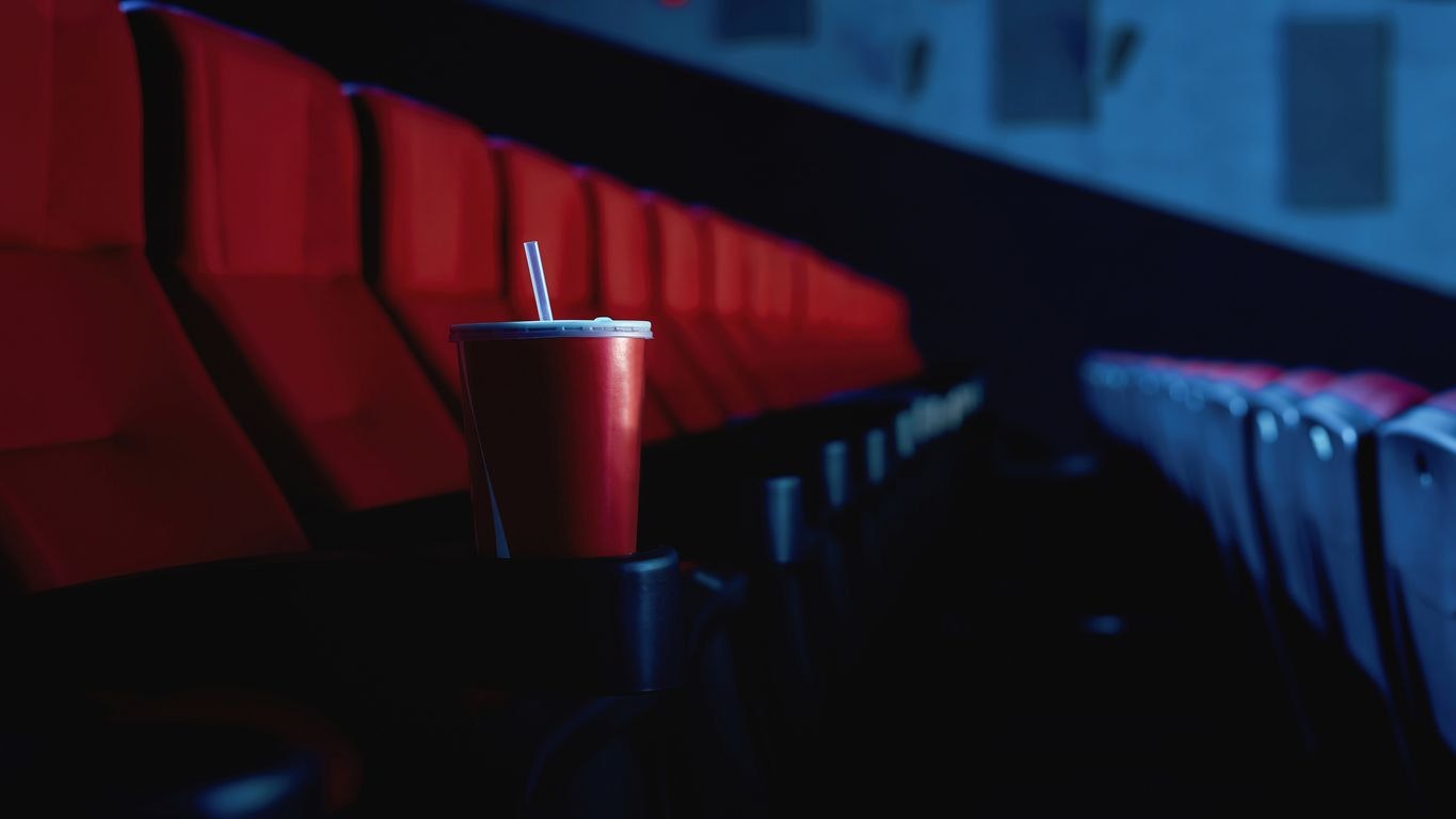 Selective focus on empty disposal cup of soda with red cinema seats in the background. Web Banner