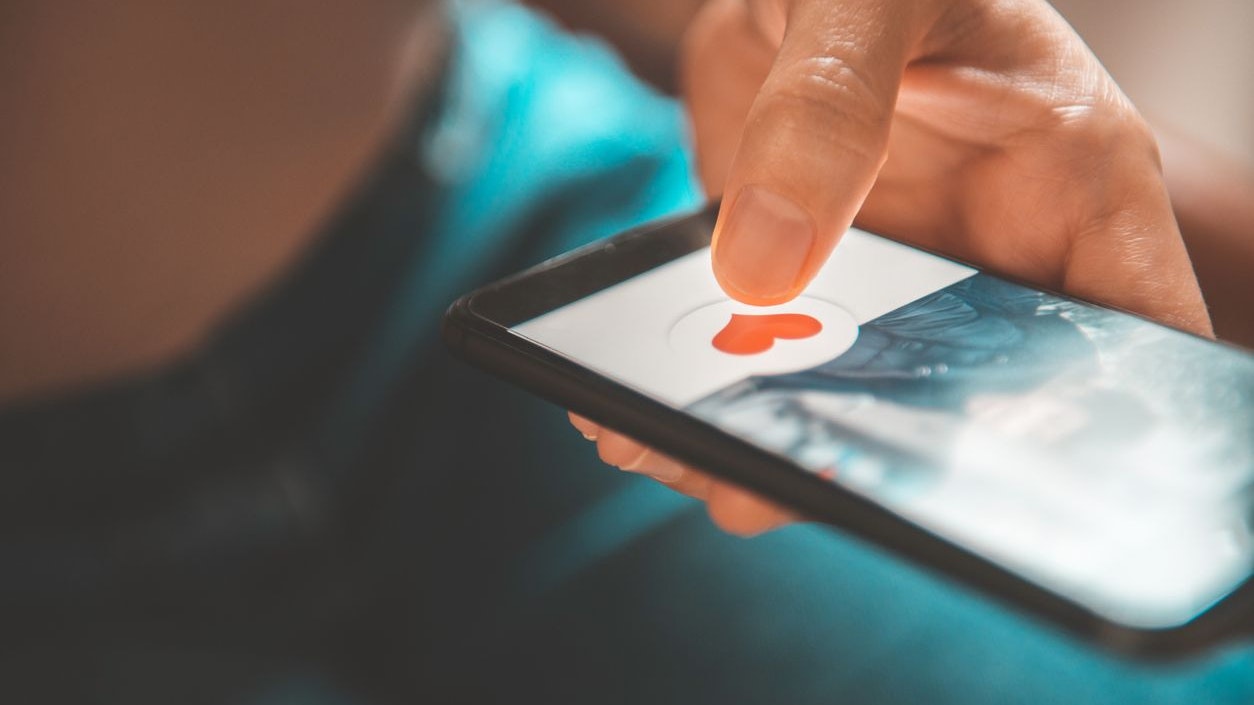 Finger of woman pushing heart icon on screen in mobile smartphone application. Online dating app, valentine's day concept.