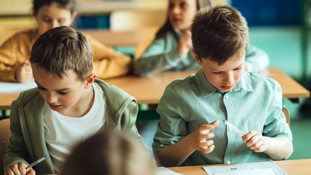 Schoolboy writing in workbook at desk in classroom. Elementary school students sitting at desk and studying in class.