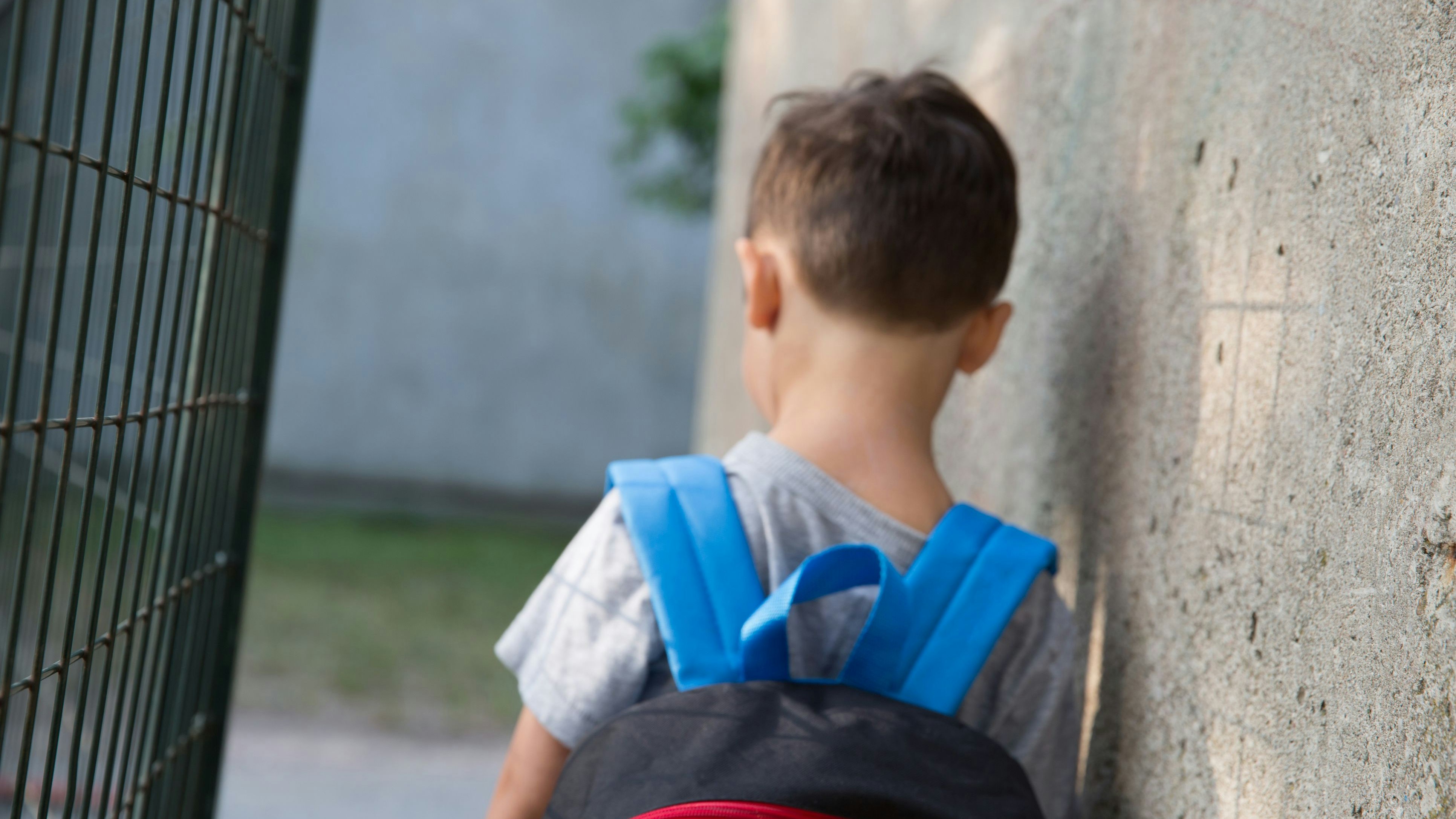 Little boy slightly out of focus and blurred with his back to the camera wearing a backpack in the schoolyard