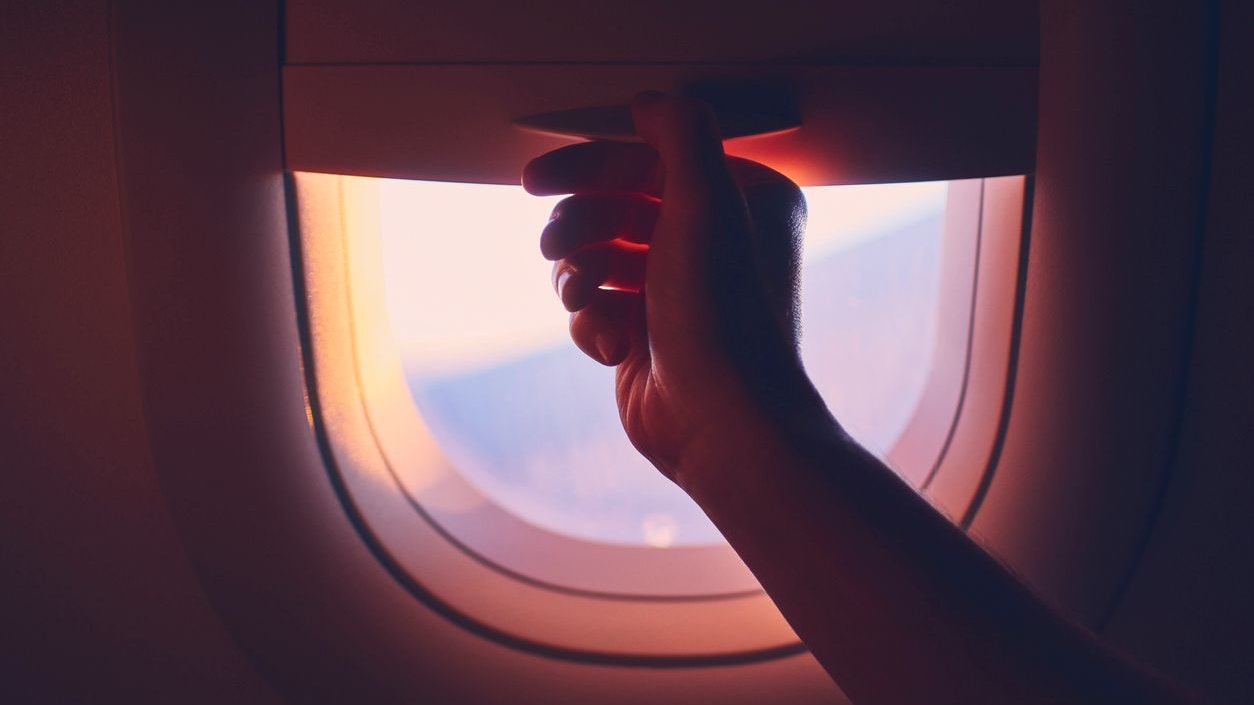 Travel by airplane. Hand pulling down or up window blinds during flight.