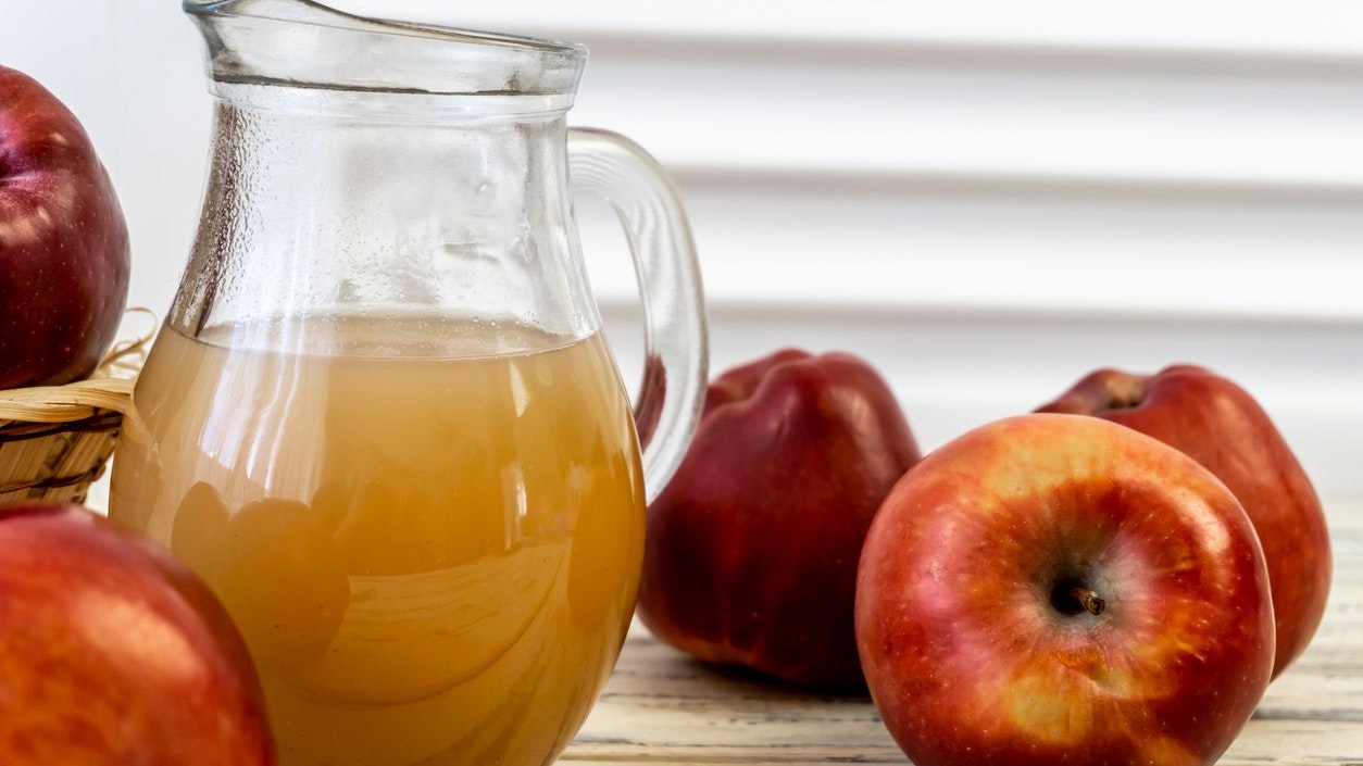 Red apples in a basket and apple juice in a jug on a wooden table