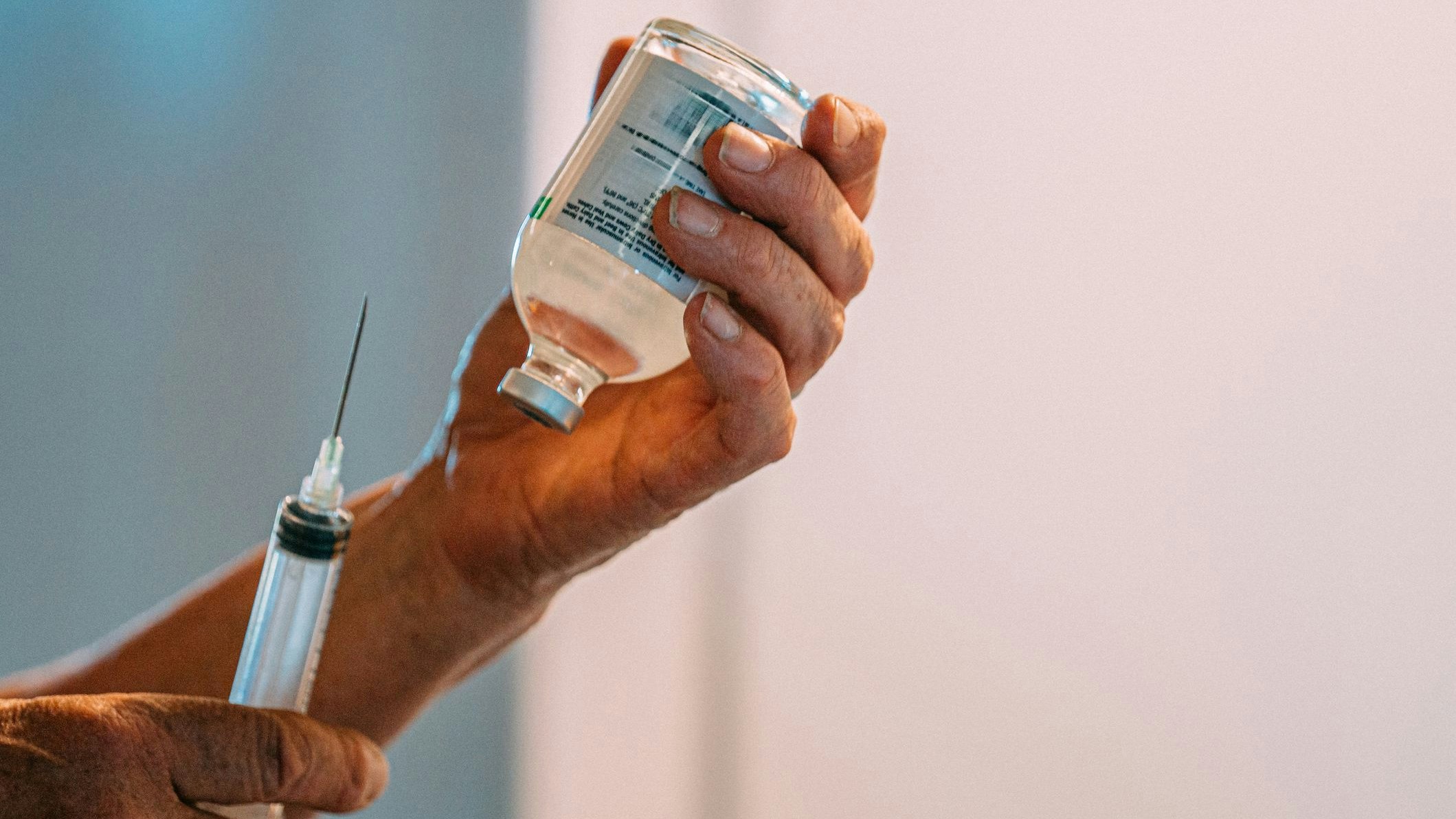 Close-up shot of Caucasian veterinarian woman getting ready to draw clear liquid medication from a glass vaccine vial container with a large hypodermic syringe indoors at an animal hospital