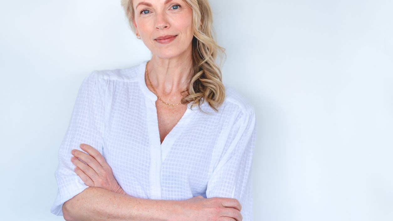 Attractive Mature woman looking strong and confident and relaxing and looking at the camera. She is standing against a white wall with her arms crossed