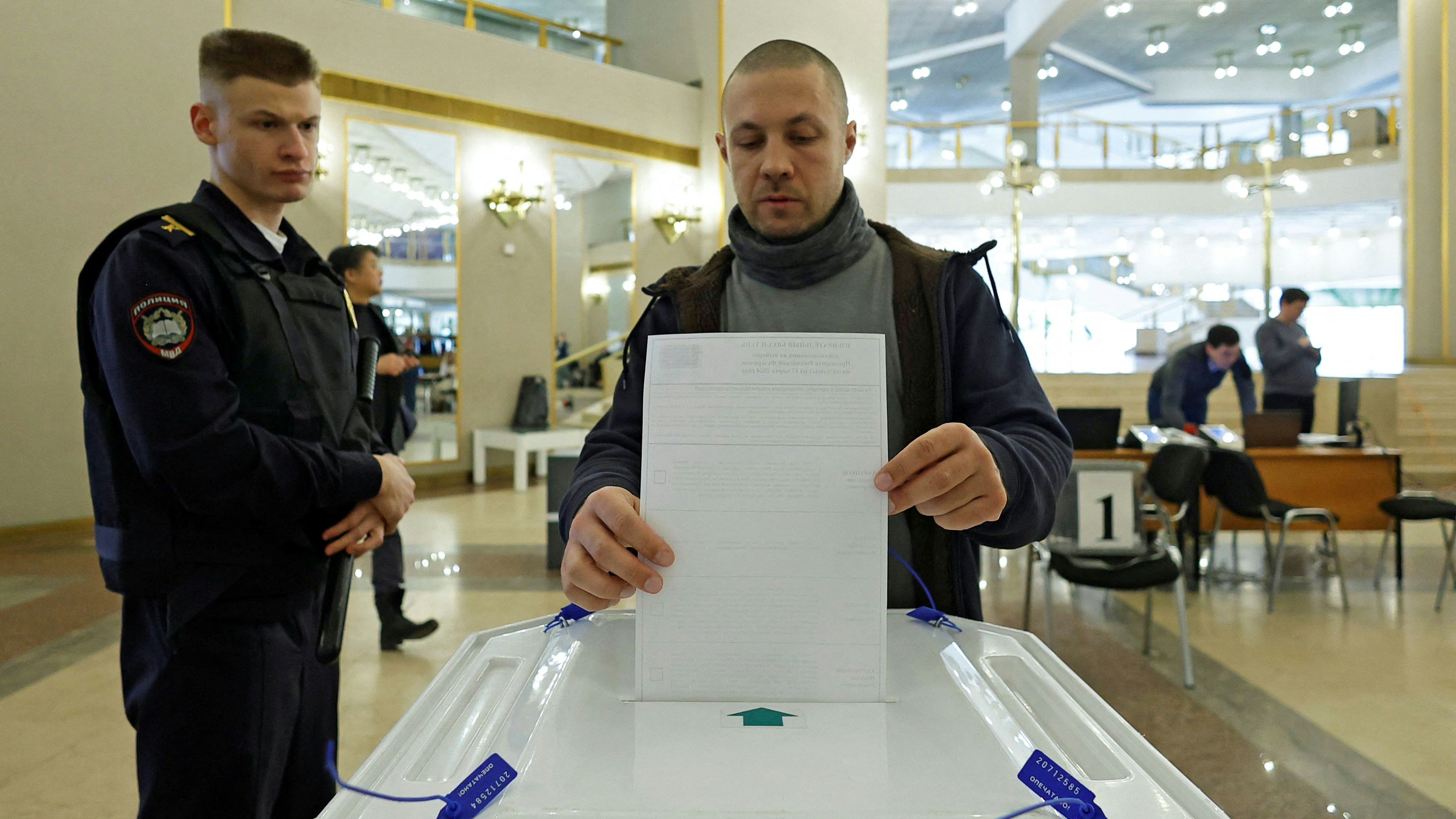 Ein russischer Wähler gibt seine Stimme ab. Dabei wird er von einem Sicherheitsorgan beobachtet.