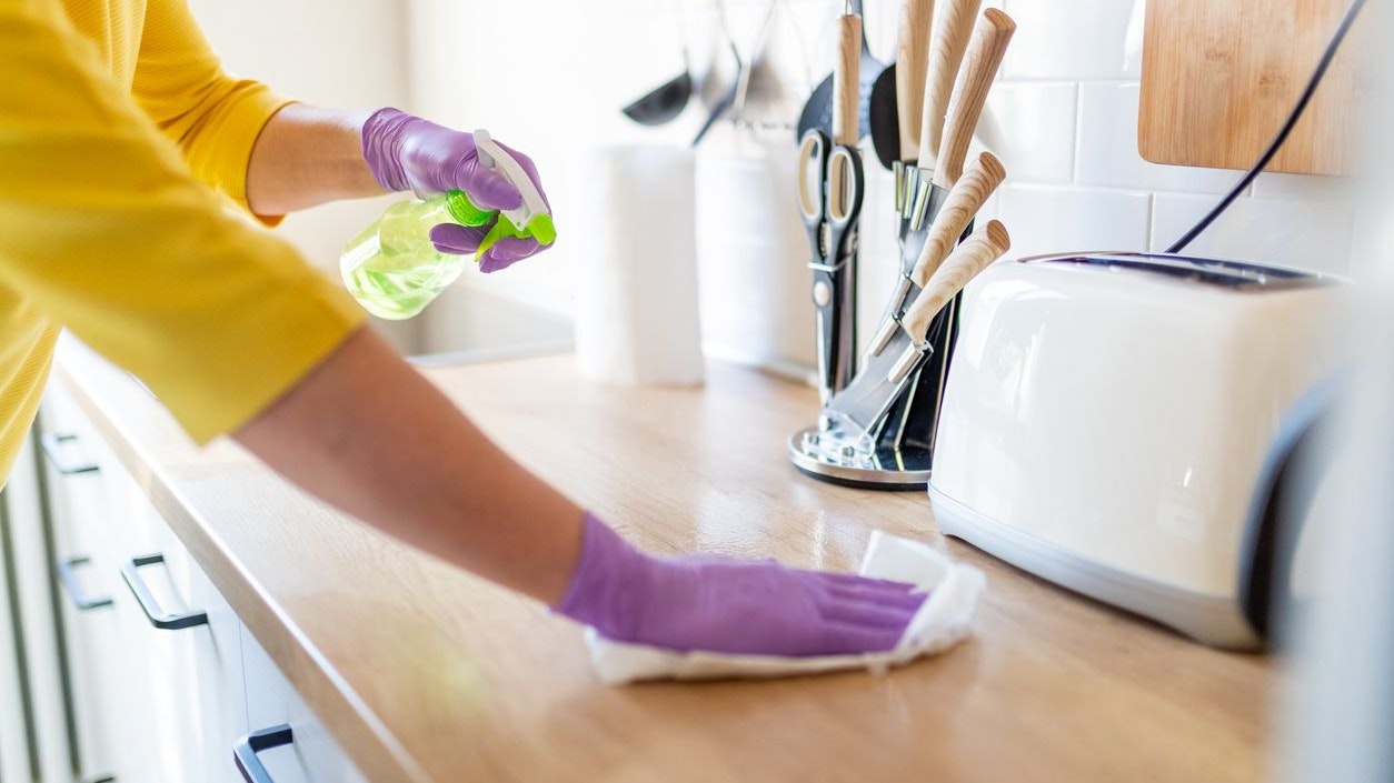 Hands in gloves disinfecting kitchen counter and wiping with paper towel against viruses