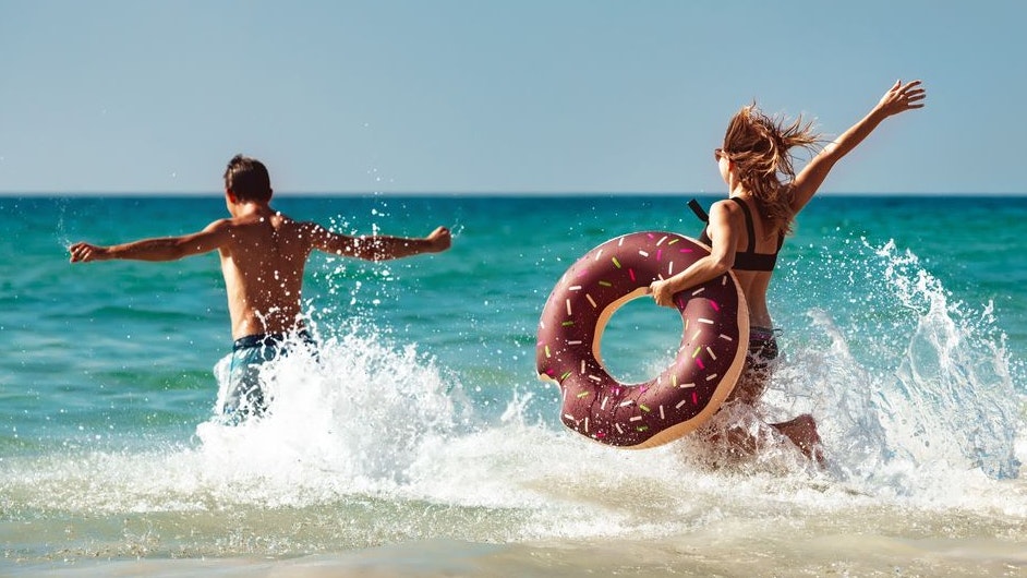 Happy young couple are having fun with inflatable donut at sea beach. Tropical vacations concept