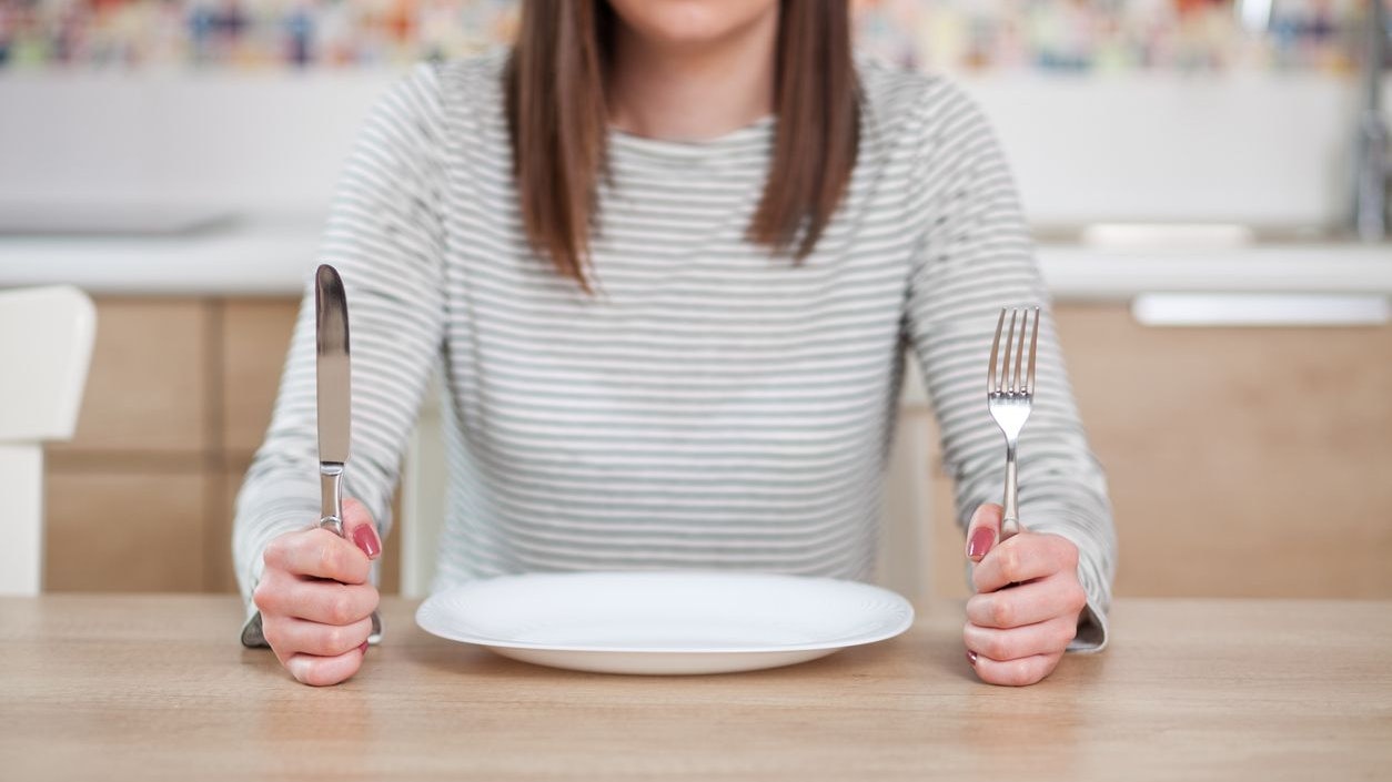 Displeased young woman sitting at the empty plate. Shallow depth of field, focus on foreground