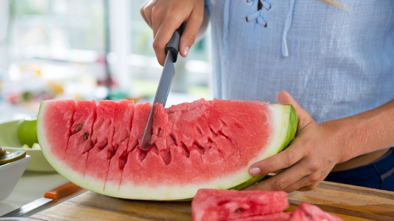 Mid-section of woman cutting fruits on chopping board against white background