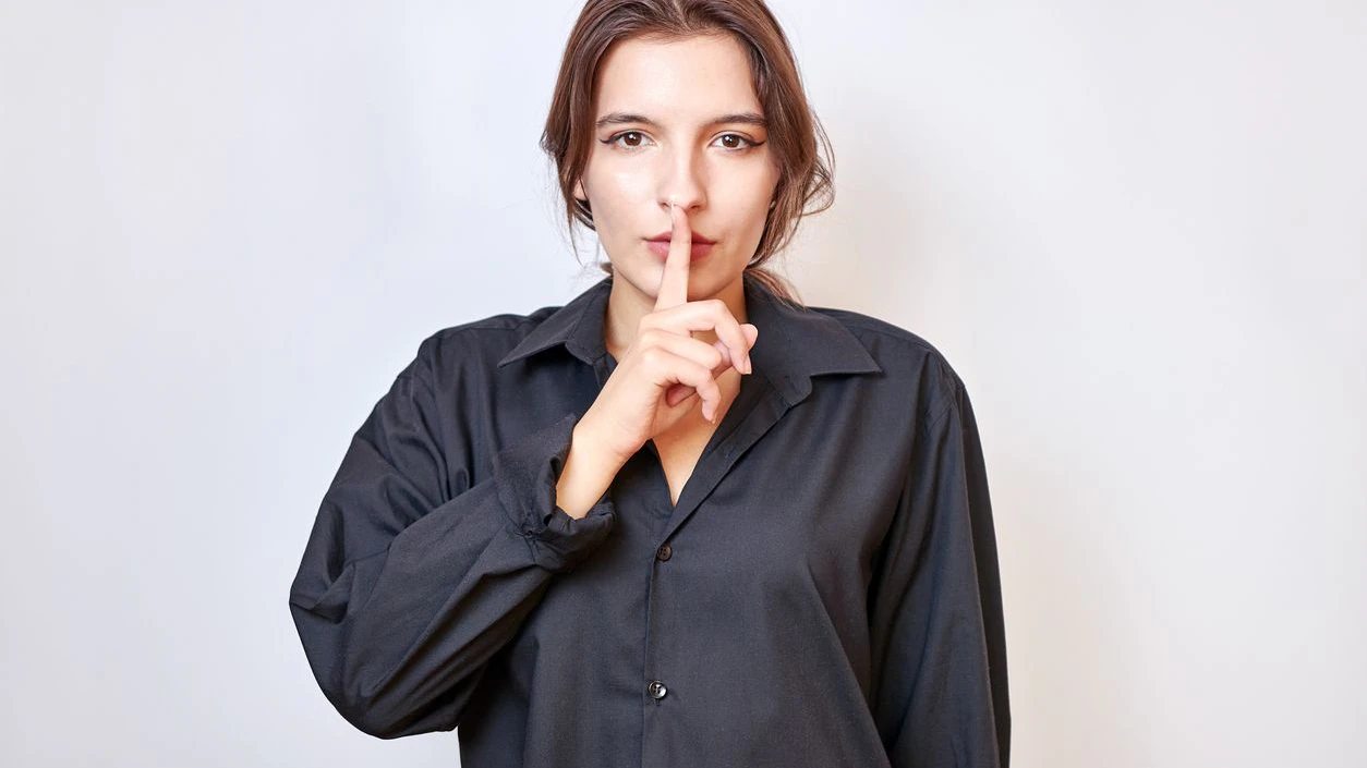 A beautiful girl shows a gesture with a finger near her lips, thereby indicating to be quiet.