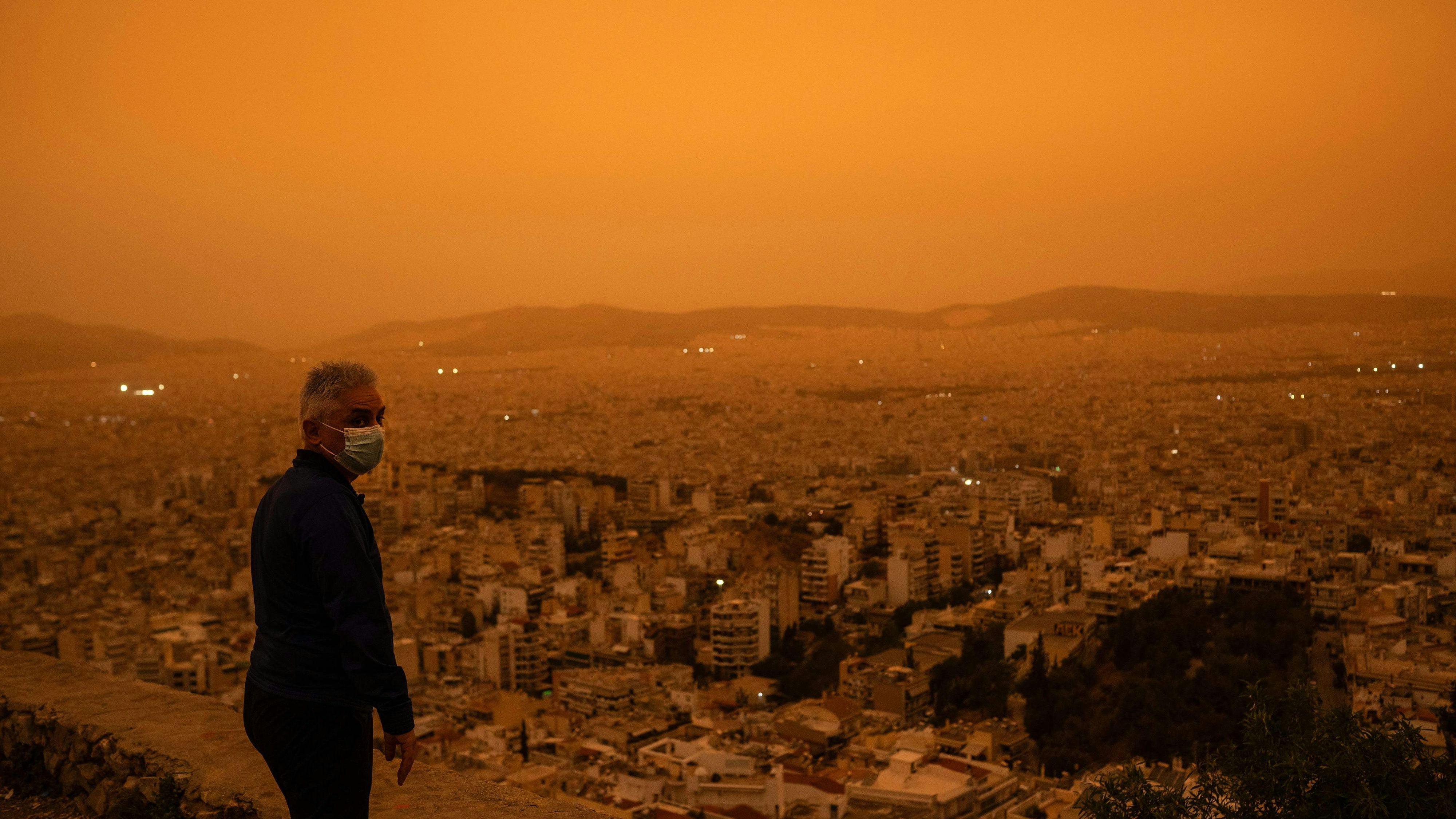 Download von www.picturedesk.com am 25.04.2024 (16:51).  A man wearing a face mask looks down on the city of Athens from Tourkovounia hill, as southerly winds carry waves of Saharan dust to the city, in Athens, on April 23, 2024. Clouds of dust blown in from the Sahara covered Athens and other Greek cities on April 23, 2024, one of the worst such episodes to hit the country since 2018, officials said. The yellow-orange haze smothered several regions, limiting visibility and prompting warnings of breathing risks from the authorities. (Photo by Angelos TZORTZINIS / AFP) - 20240423_PD7818 - Rechteinfo: Rights Managed (RM) Nur für redaktionelle Nutzung! Werbliche Nutzung erfordert Freigabe: bitte schicken Sie uns eine Anfrage.