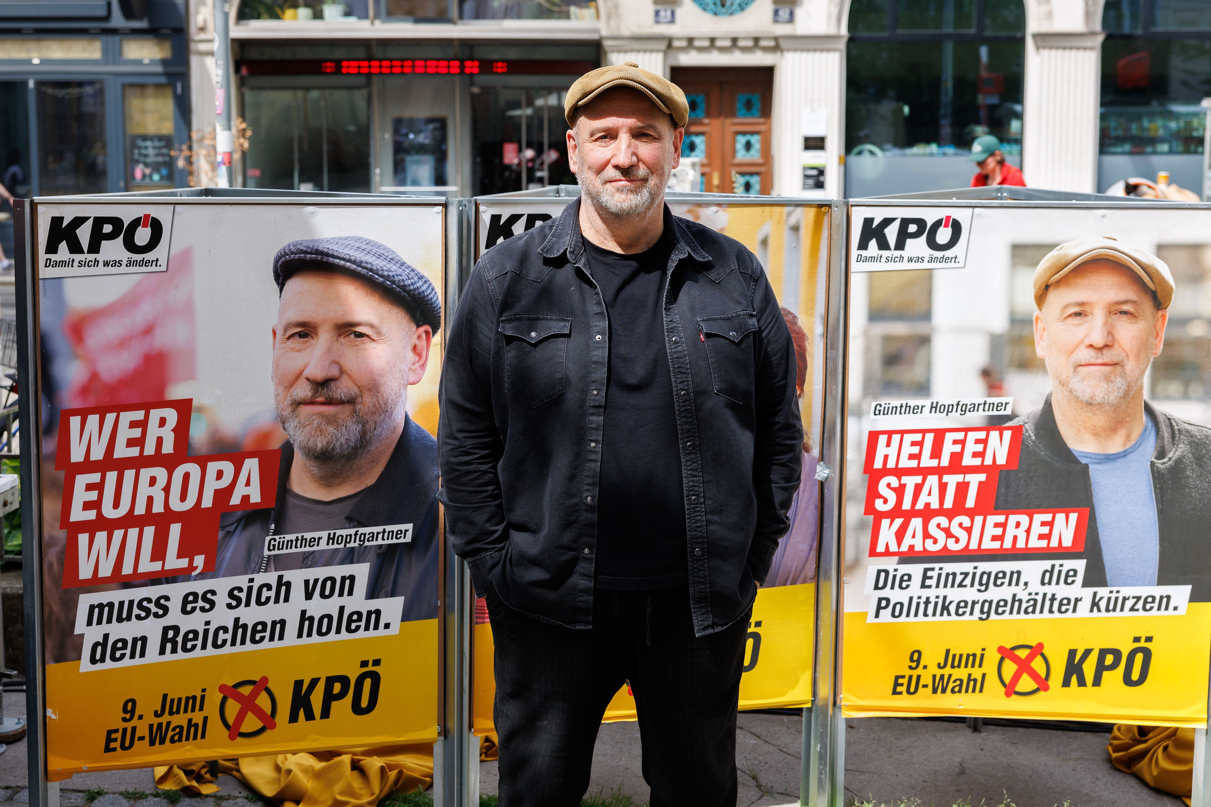 KPÖ-Spitzenkandidat Günther Hopfgarten posiert vor seinen Plakaten für den EU-Wahlkampf.