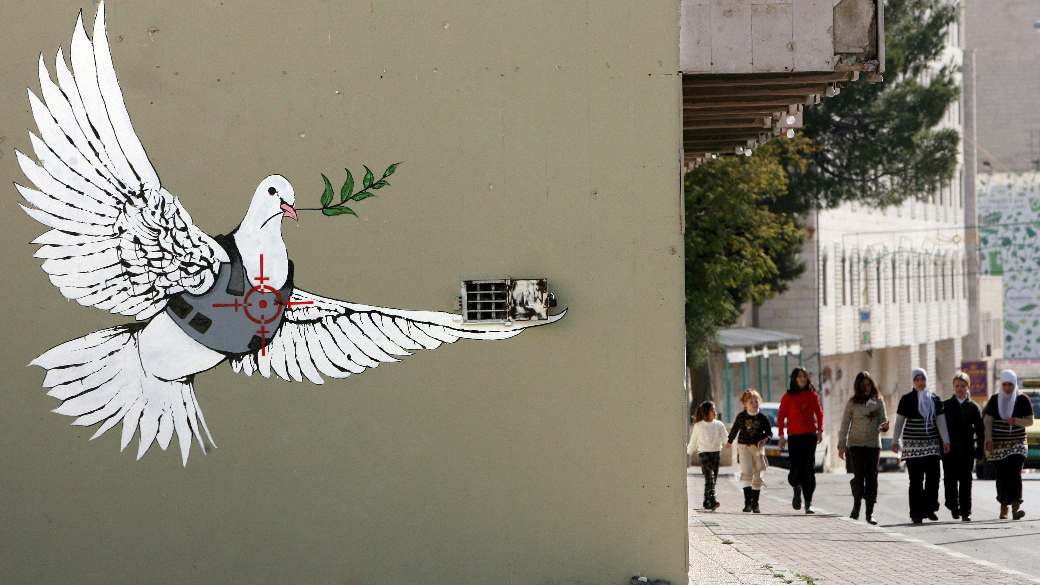 Download von www.picturedesk.com am 06.05.2024 (19:10).  epa01205127 Palestinian girls walk down a main street in the West Bank town of Bethlehem on 19 December 2007 near a large painting of a Peace dove in a flak jacket as a sniper takes aim at the bird's heart. Many graffiti artists have decorated Bethlehem, the town where Jesus was born on Christmas, and it controversial 'separation barrier,' or wall, with political graffiti having to do with the Israeli wall and the 'occupation of Palestine.' EPA/JIM HOLLANDER - 20071219_PD2544 - Rechteinfo: Rights Managed (RM)