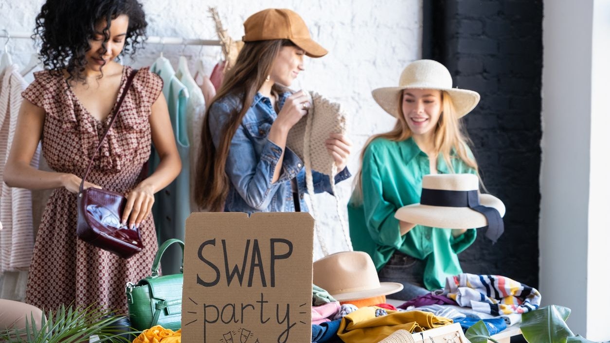 Happy women try on things at second hand store. Choose casual clothes, shoes, hats, bags, jewellery. Idea of exchange old wardrobe. Eco friendly cloth concept. Zero waste shopping, reduce and reuse