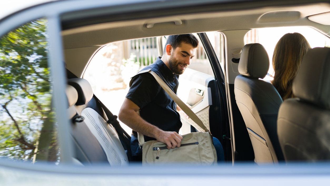 Handsome male passenger smiling and getting on a rideshare car while talking to the female driver