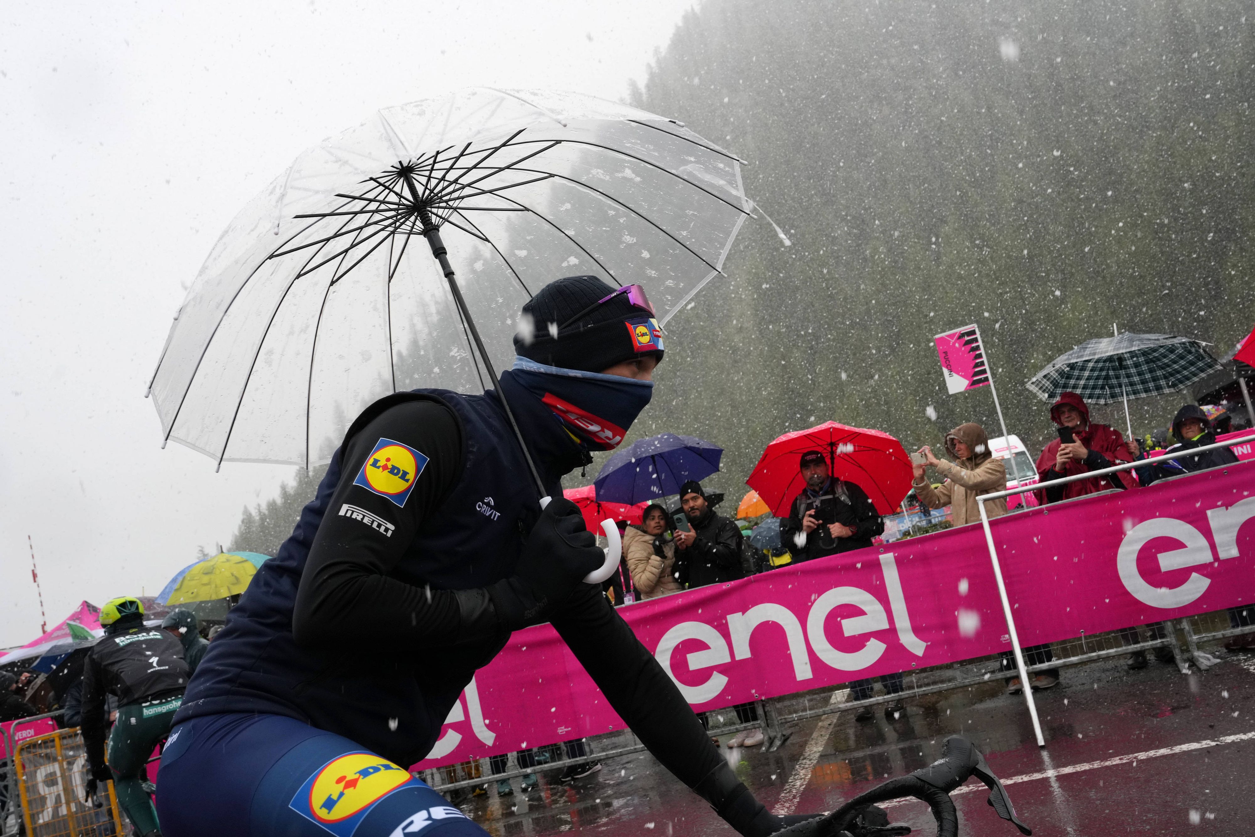 Rad-Star vermummt und mit Regenschirm gegen die Schneeflocken.