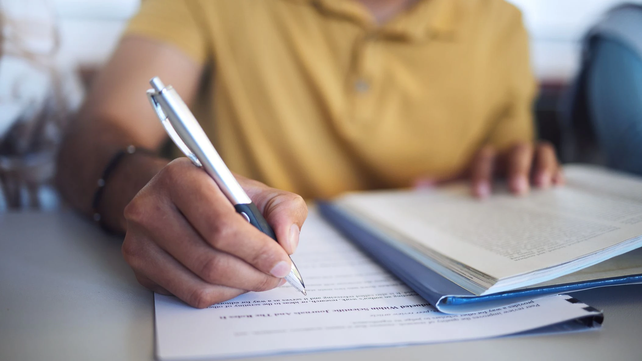 Student exam, college test and hand of man writing question paper in classroom for education, book research and knowledge for scholarship registration. Person at university to study, learn and write