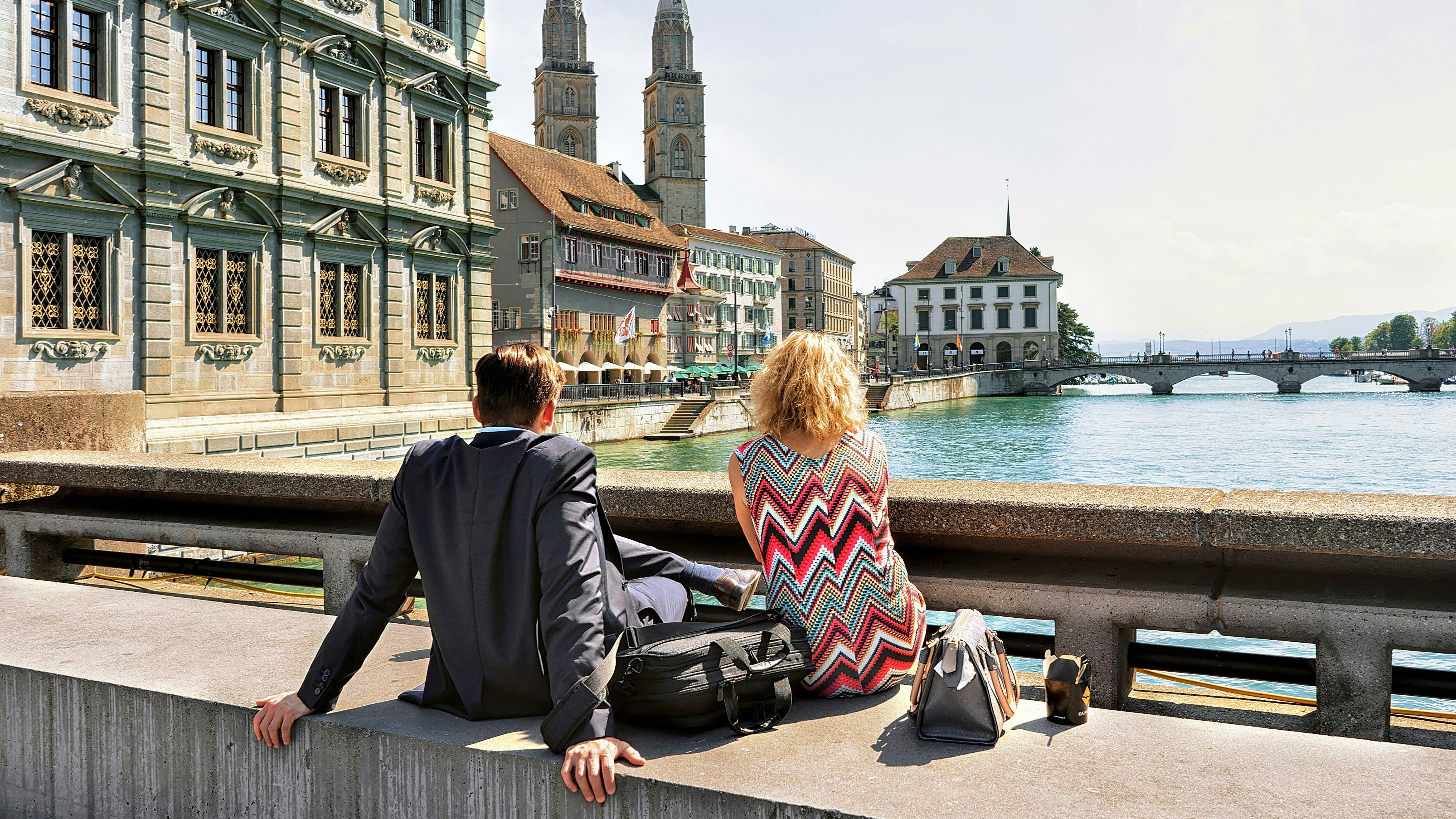 Zurich, Switzerland - September 2, 2016: Romantic couple sitting at Limmat River Quay and looking at Grossmunster Church in Zurich, Switzerland