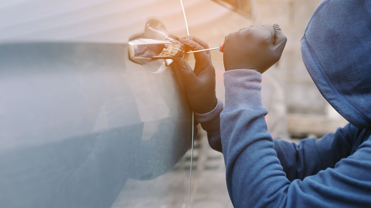 Close up car thief hand holding screwdriver tamper yank and glove black stealing automobile trying door handle to see if vehicle is unlocked  trying to break into inside.