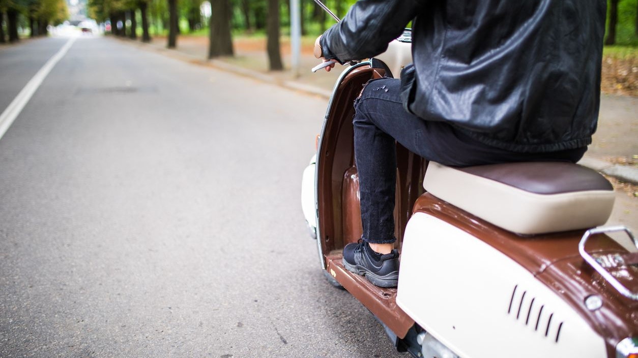 Close up portrait of young man driving scooter on street.