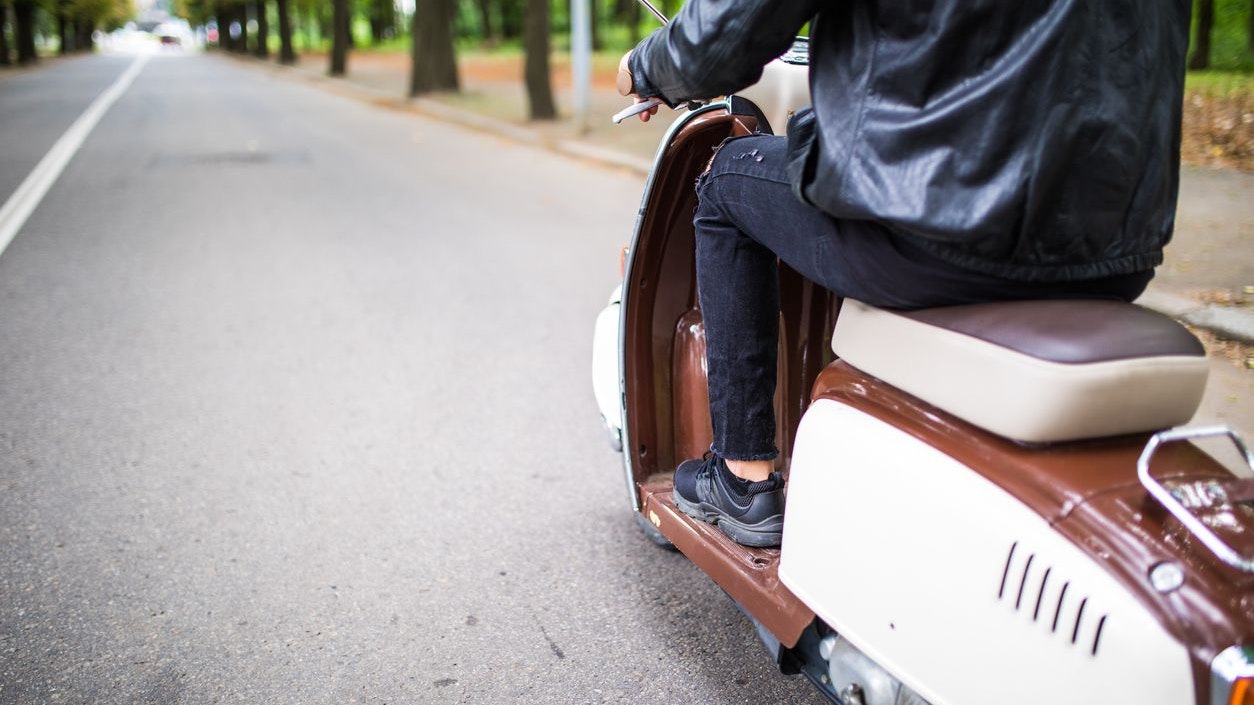 Close up portrait of young man driving scooter on street.