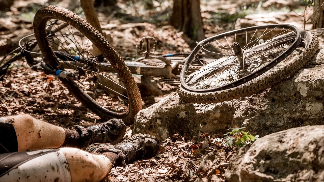 A mountain biker has an accident on his bike.